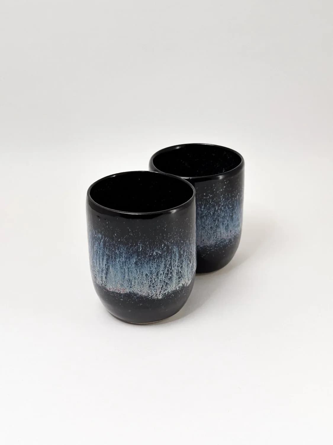 Two stacked black ceramic mugs with ring handles and galaxy-effect glaze