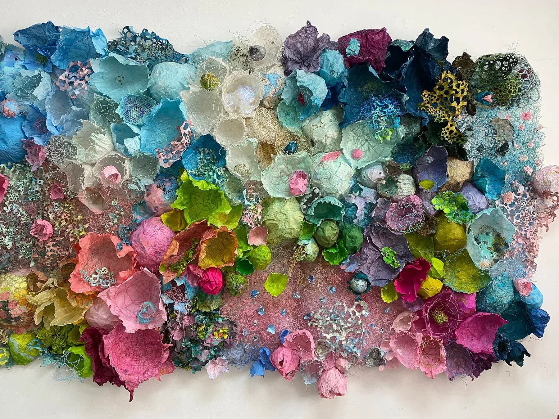 Detailed view of textured paper sculpture with blue, aqua, pink and cream organic forms and wire mesh