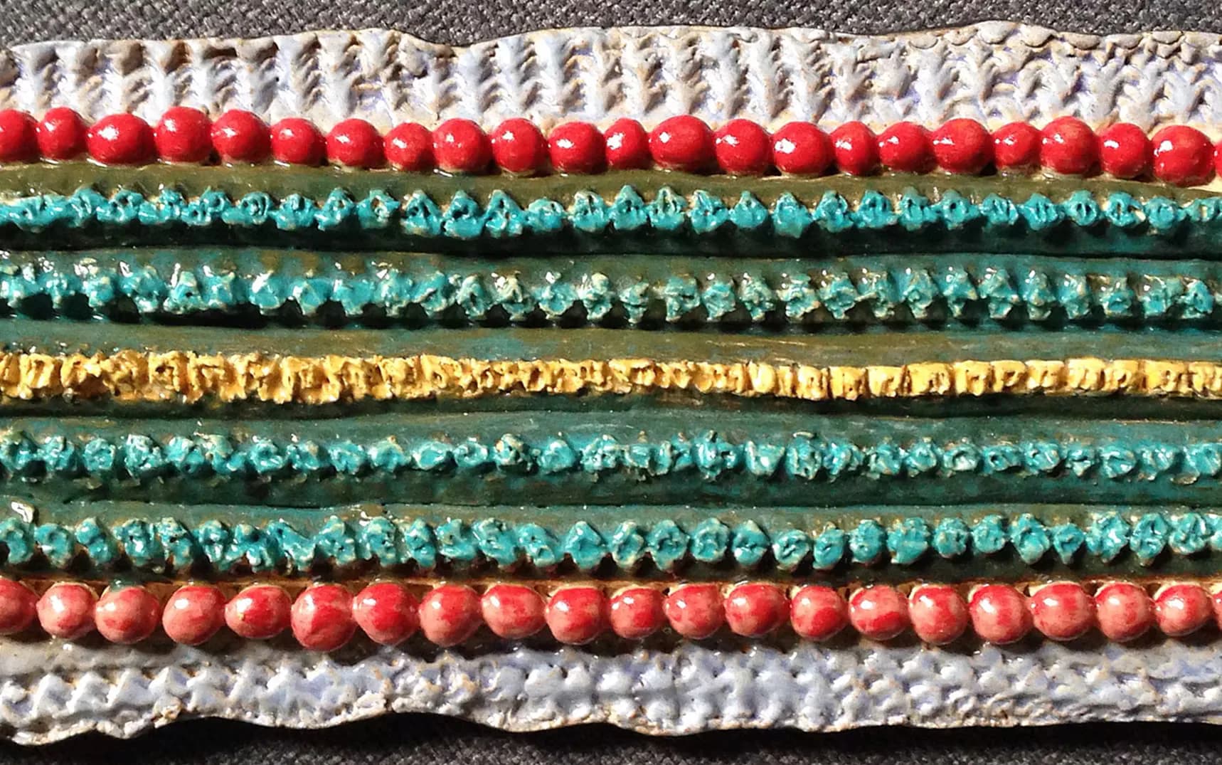 Textured ceramic wall piece with horizontal bands of red beads, turquoise, yellow, and white glazed elements