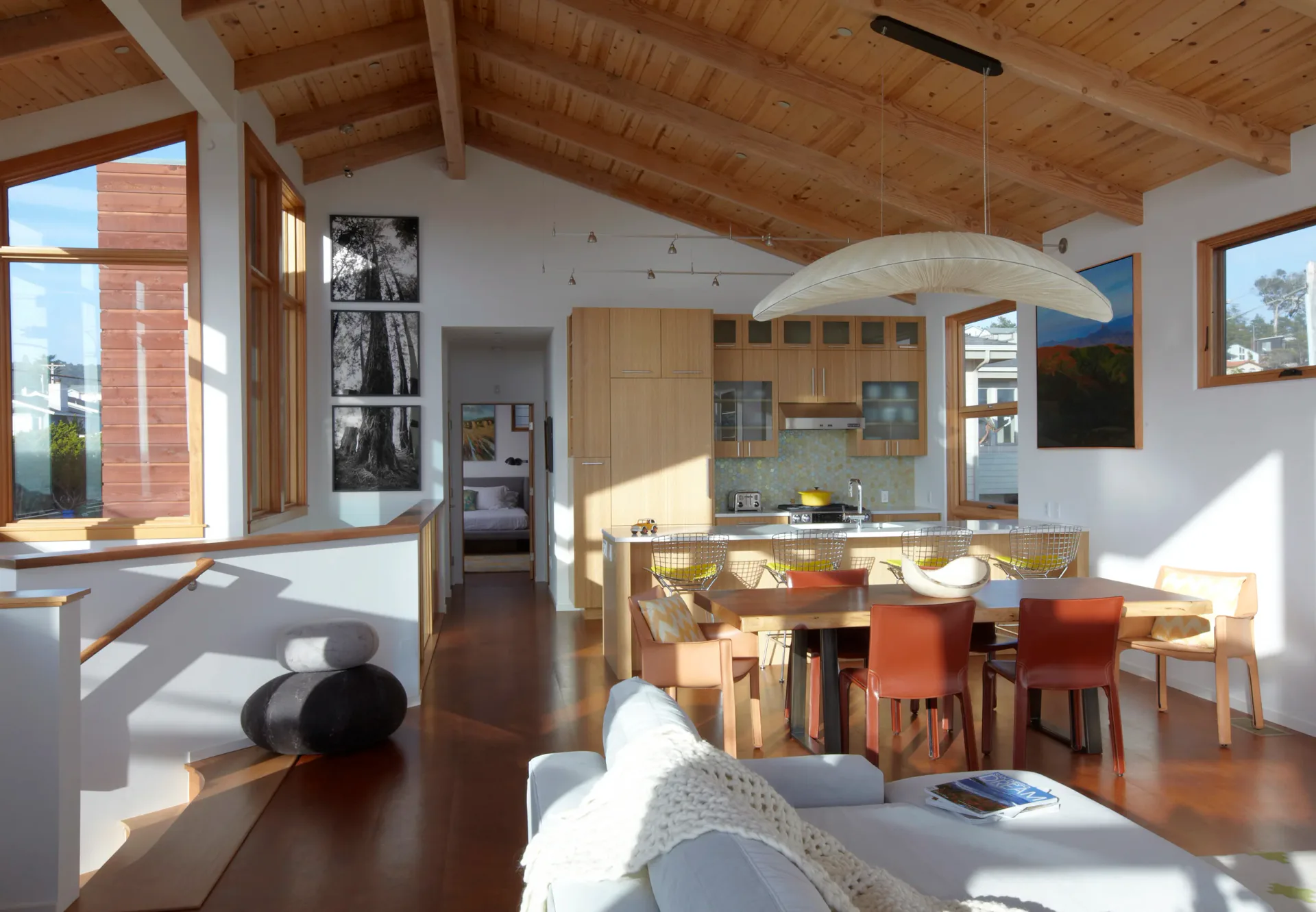 Photograph of a modern open-plan residential space with wooden beams, kitchen, dining area, and living room flooded with natural light.