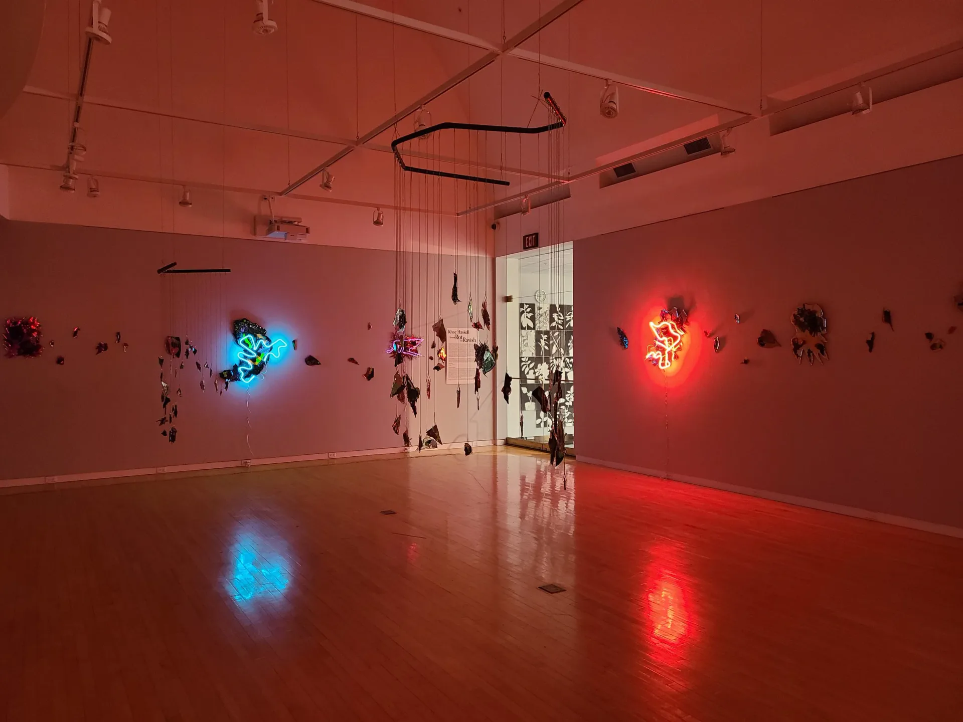 Full gallery installation view with neon sculptures, hanging mobiles, and red ambient lighting