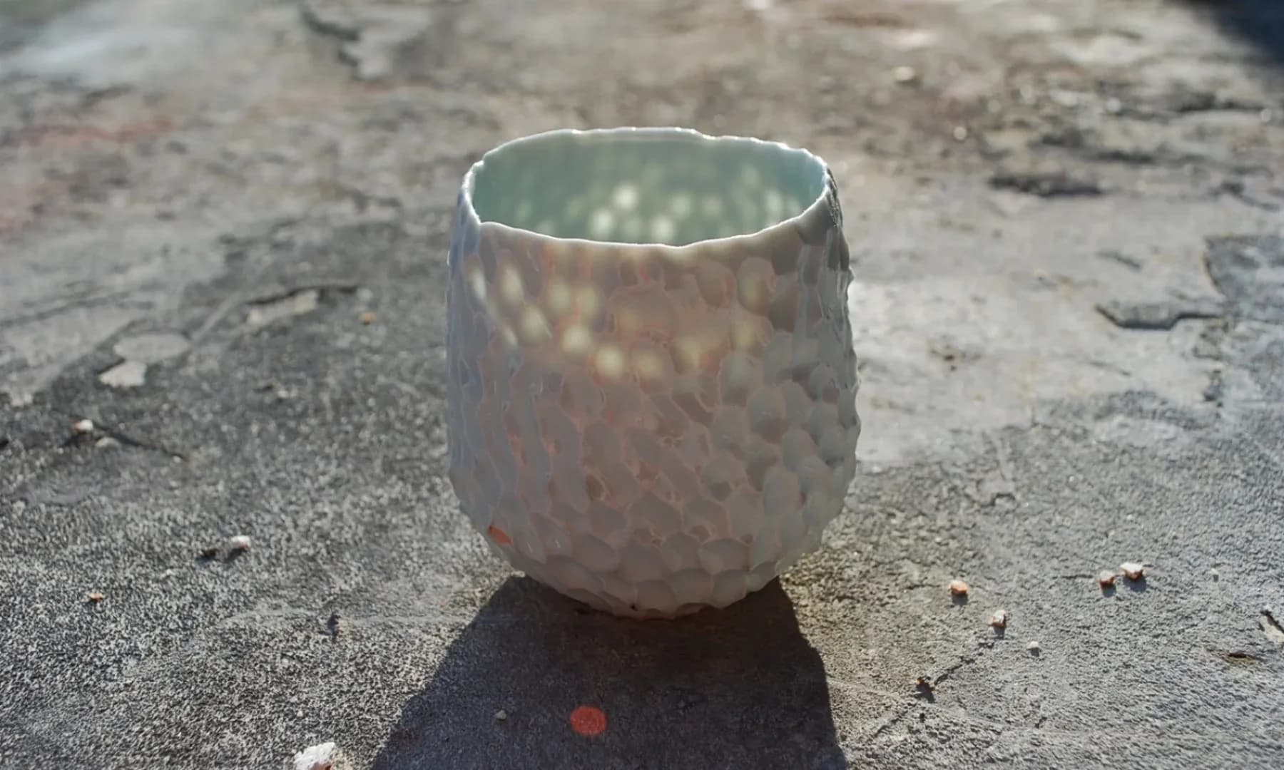 Dimpled white porcelain vessel with celadon interior glaze, photographed outdoors on concrete