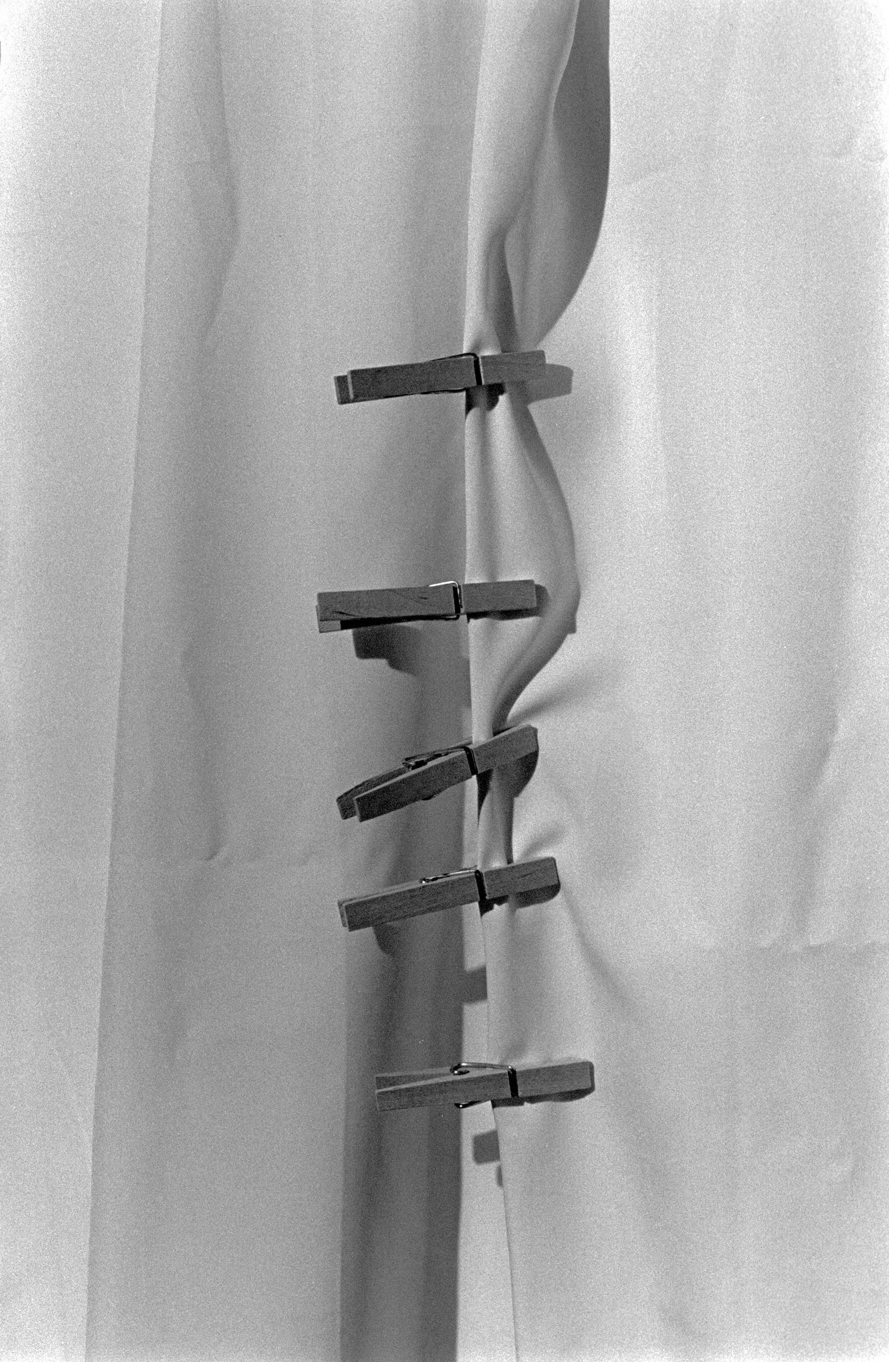 Black and white photograph of clothespins clamped along a gathered fabric fold