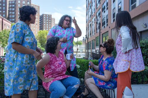 Group of five people wearing colorful patterned clothing gathered outdoors in urban setting with buildings behind them.