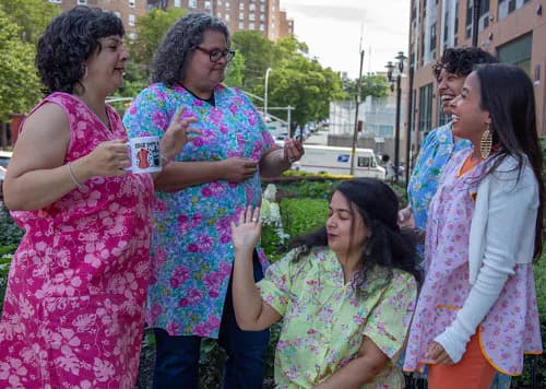 Group of five people in bright floral and colorful patterned clothing conversing outdoors in urban plaza setting.