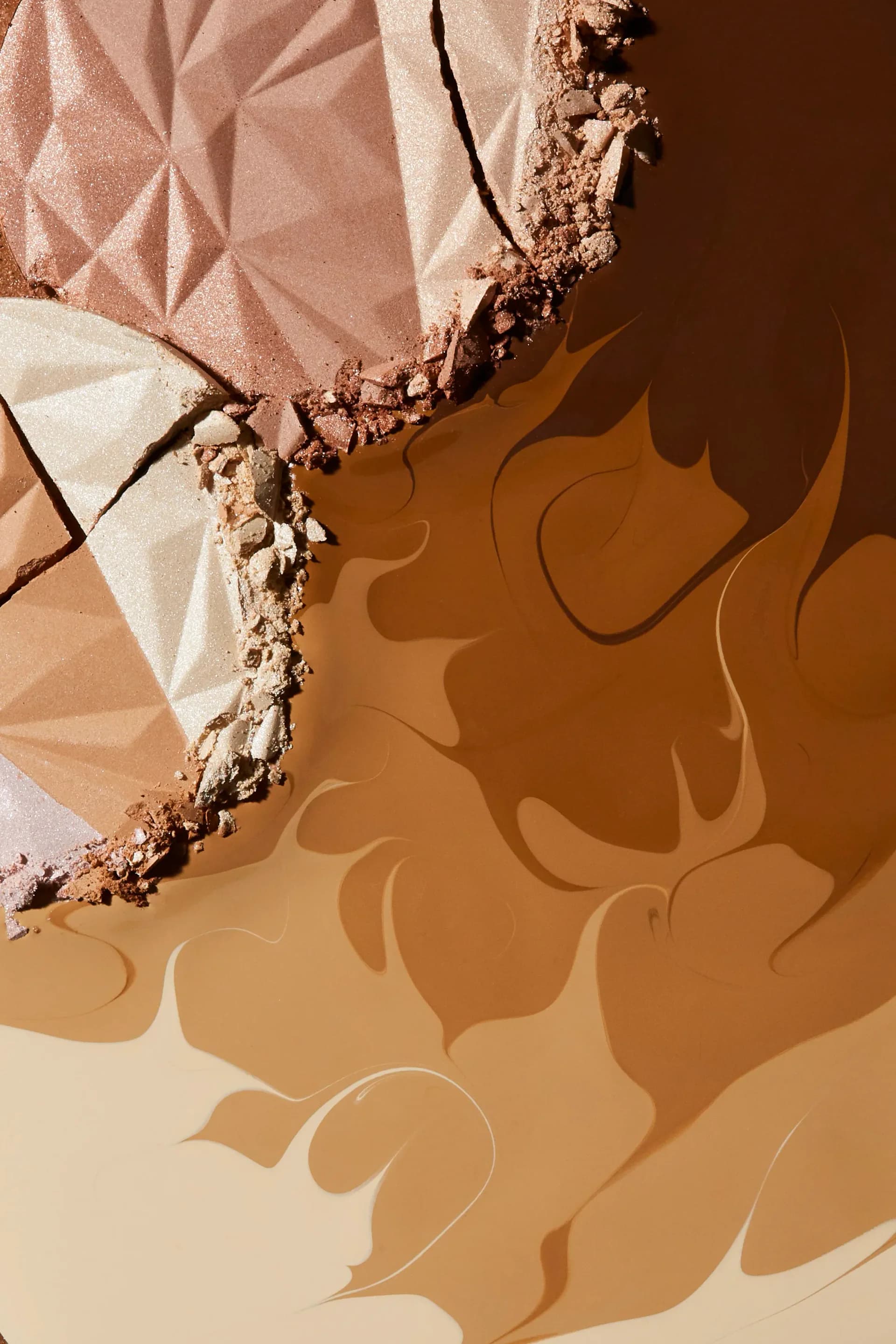 Close-up beauty photograph of shattered powder eyeshadow palette in warm bronze and nude tones with dramatic shadow.