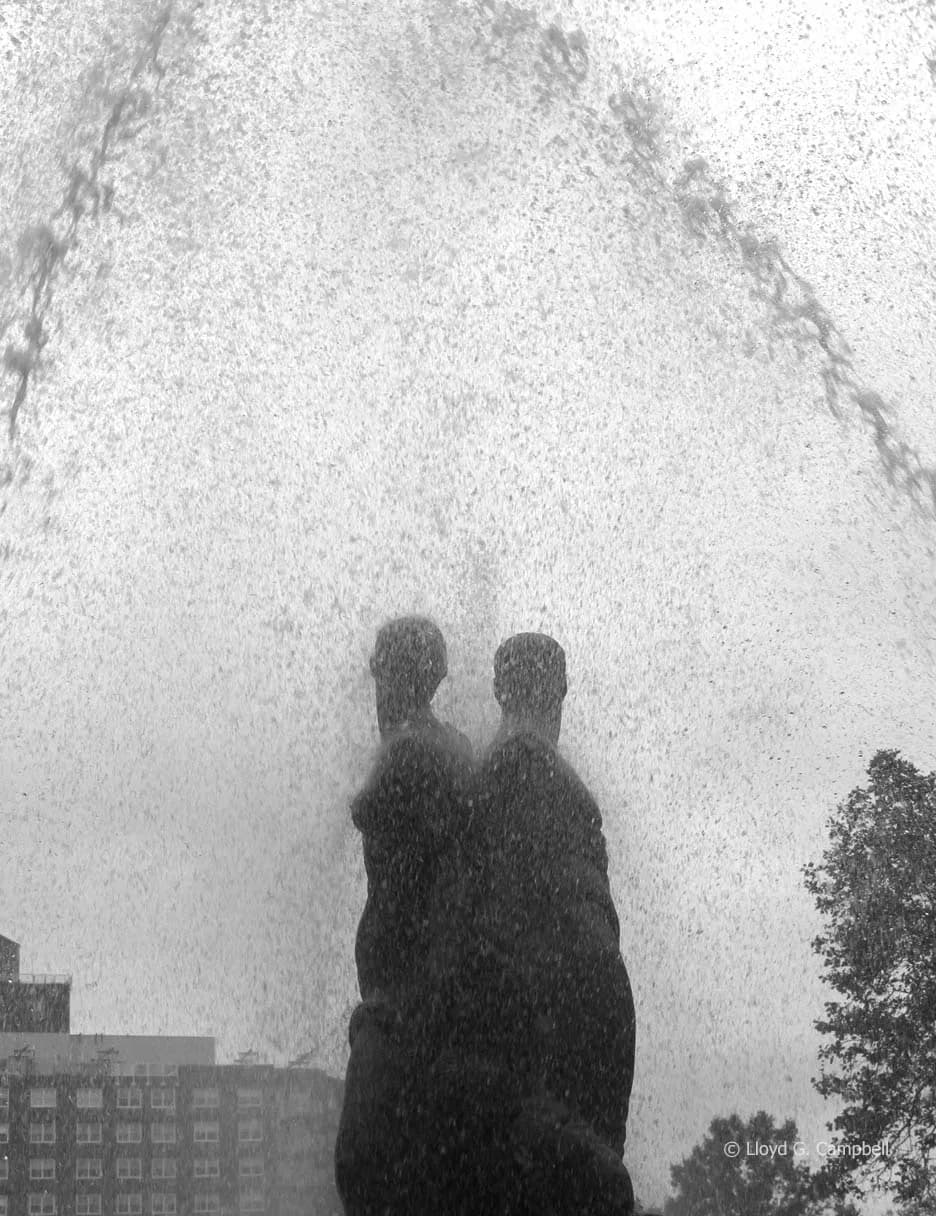 Two figures silhouetted within a cascade of fountain water, black and white photography