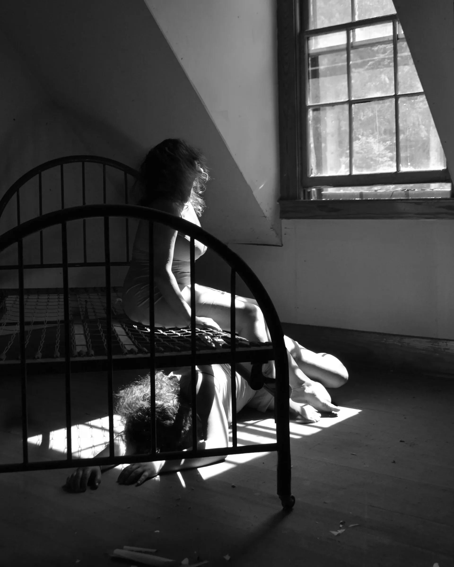 Figure seated on iron bed frame by window, dramatic black and white light
