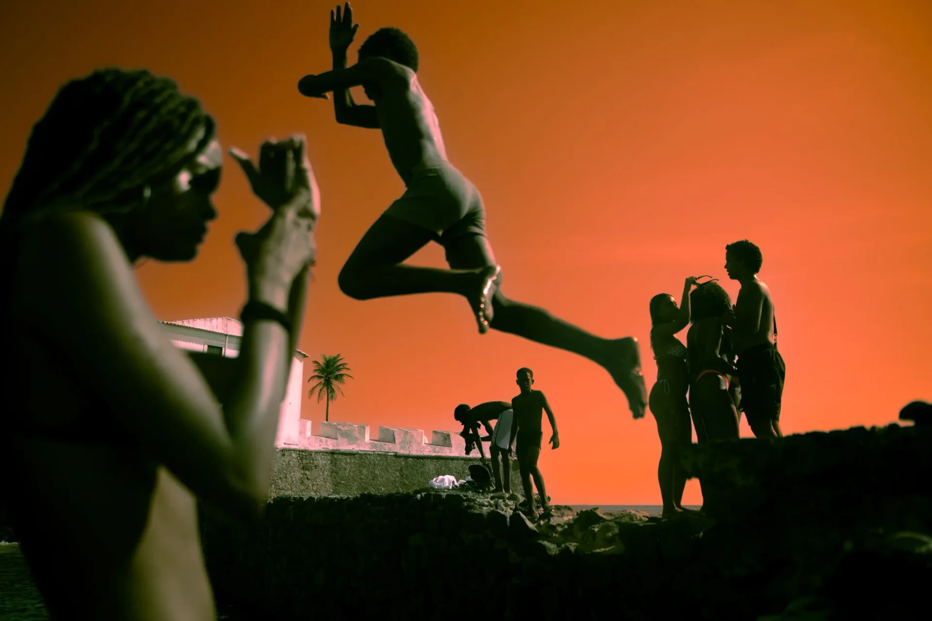 Silhouettes of children jumping against a vivid orange-red sky