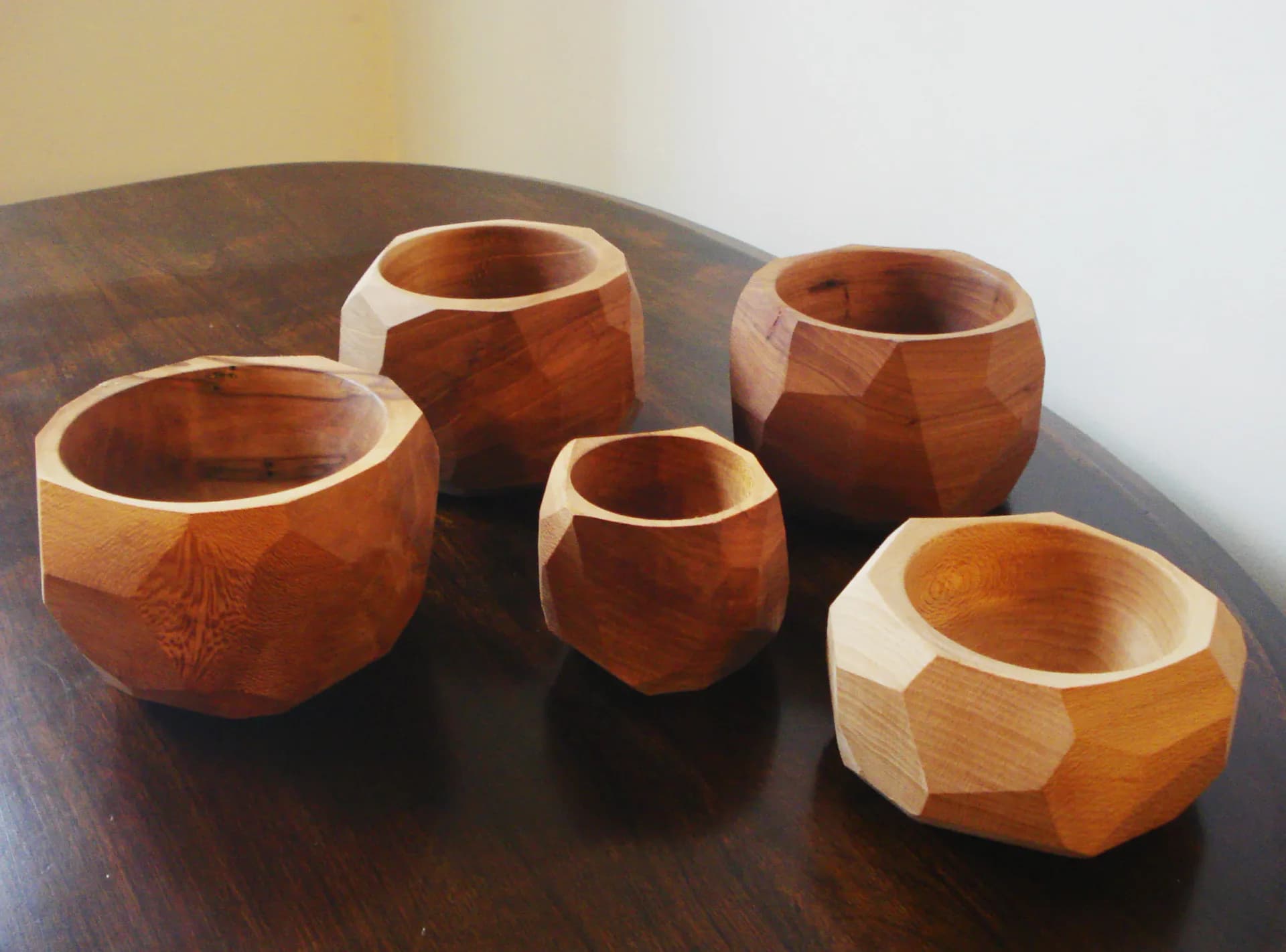Five faceted wooden bowls of varying sizes displayed on a dark wood table