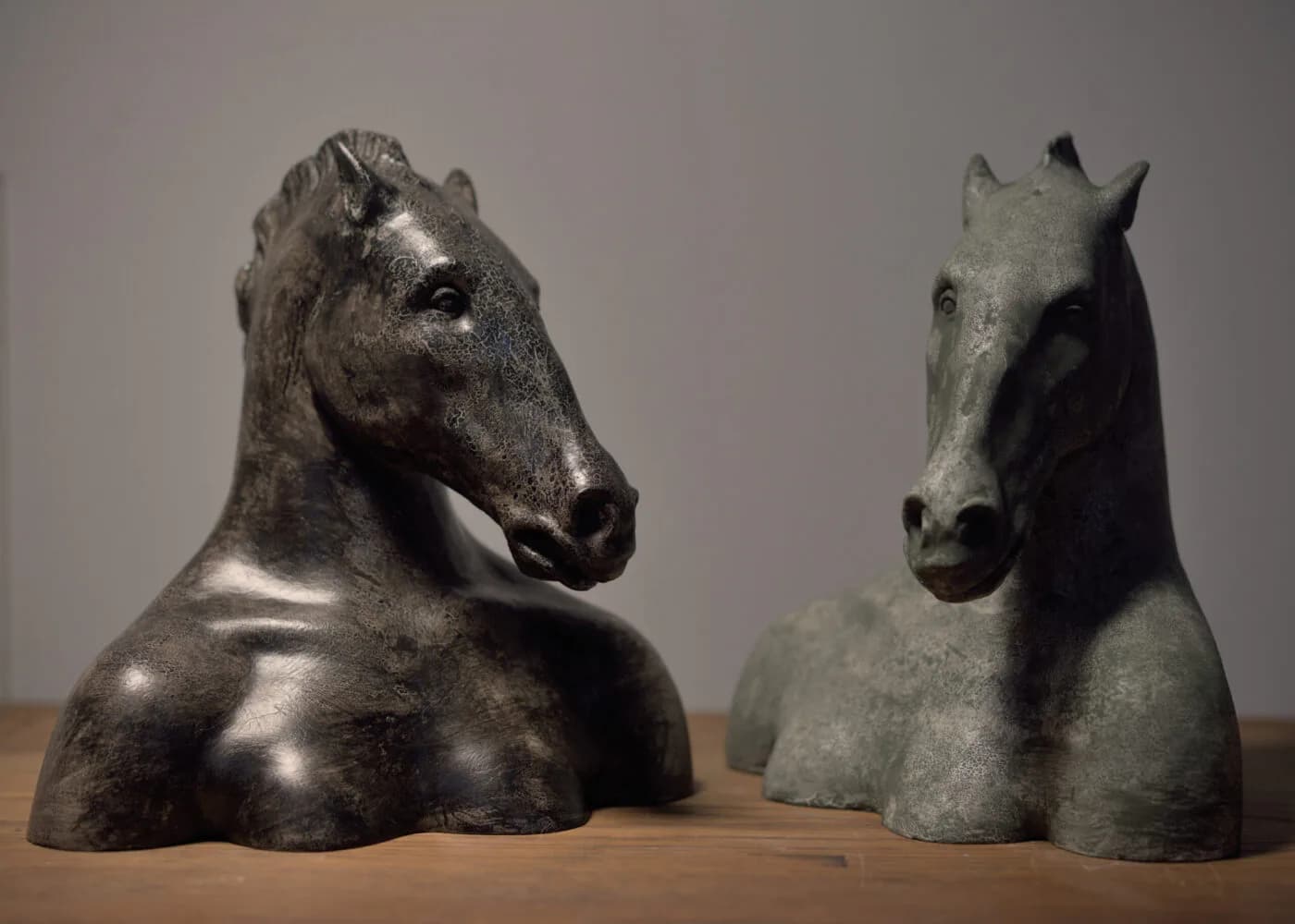 Two ceramic horse bust sculptures in dark metallic glaze displayed on wooden surface