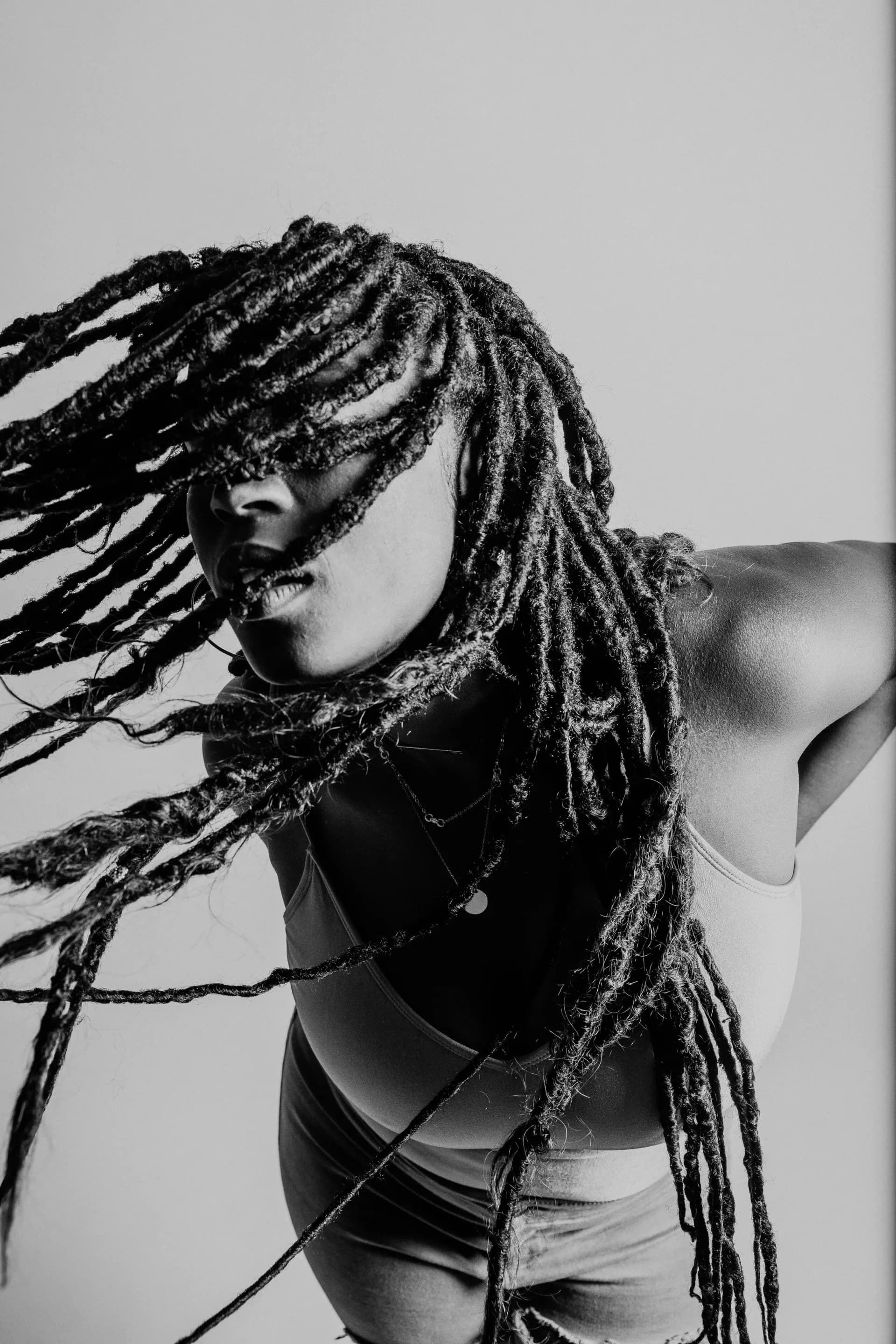 Black and white dynamic portrait of subject with flowing dreadlocks in motion against white background