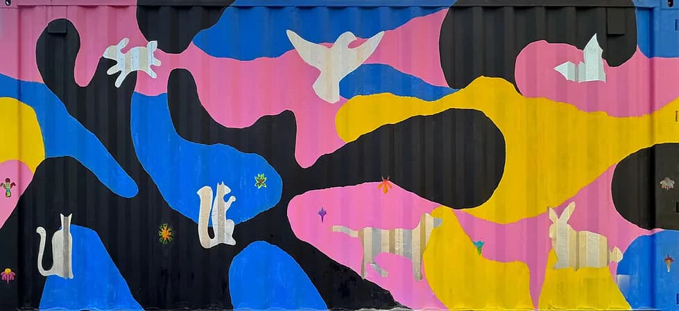 Vibrant abstract mural with organic biomorphic shapes in pink, blue, yellow, and black, featuring white animal silhouettes including rabbits and birds.