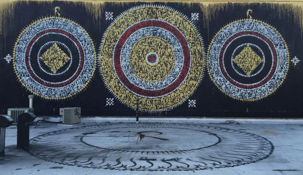 Triptych mural with three ornate circular mandala-like patterns in gold, red, and blue on dark background, with geometric floor design below.