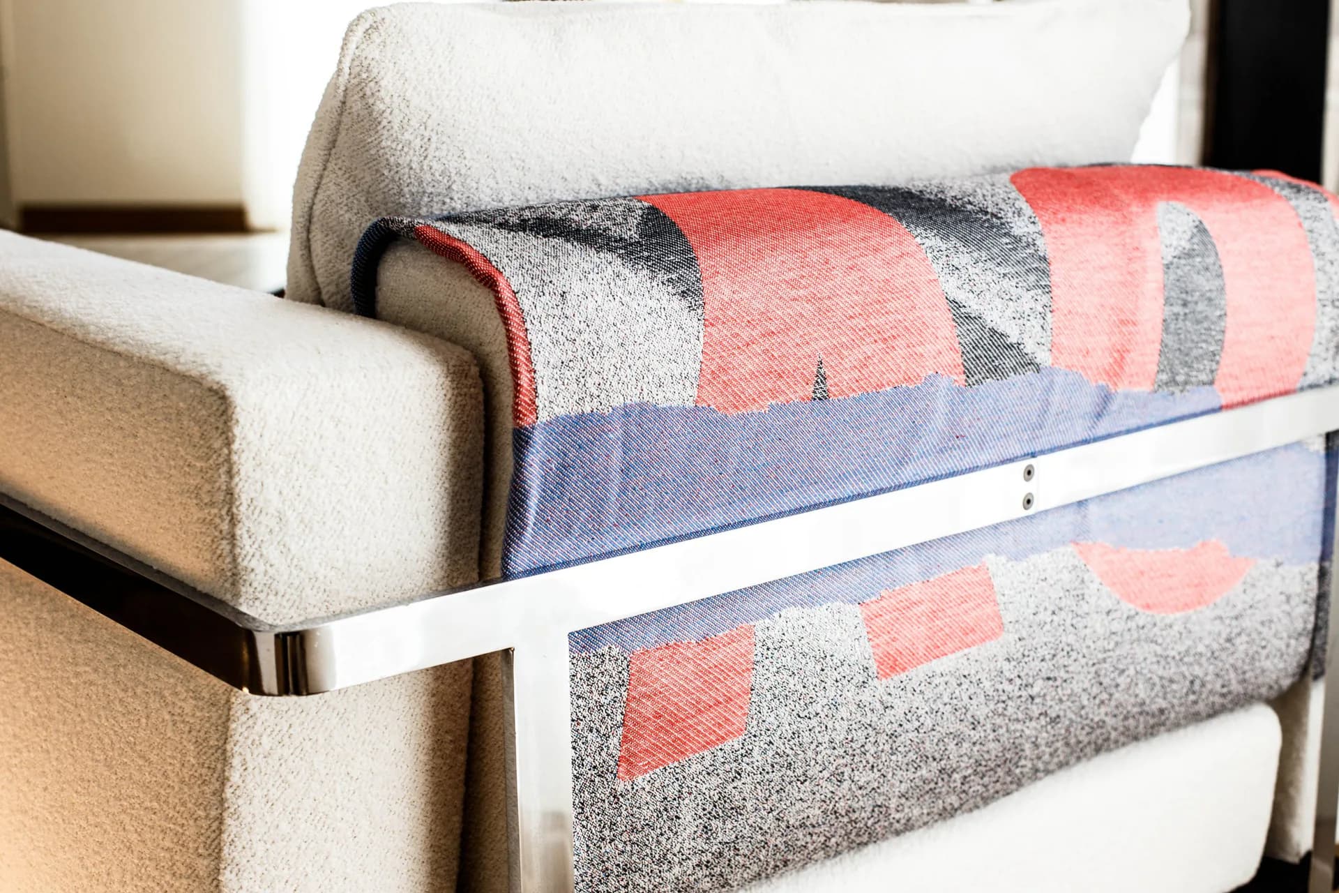 Styled photograph of folded blanket and white pillow on a modern bed frame with metallic rail, showing texture and color blocking.