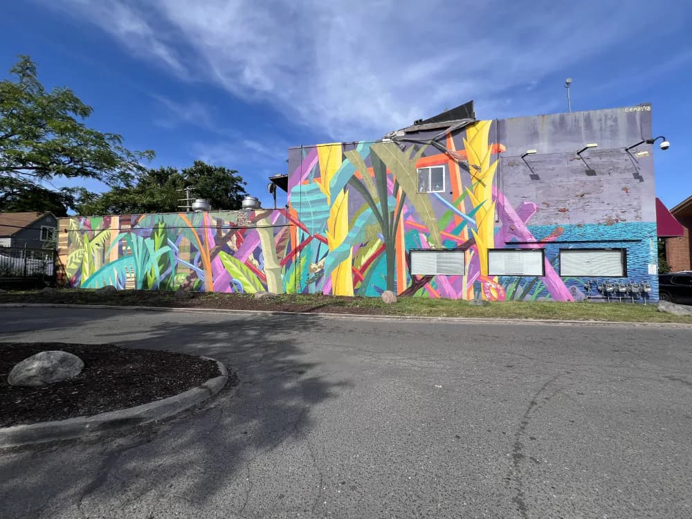 Colorful mural with abstract geometric and floral shapes in yellow, pink, green, and blue painted across multi-building exterior.