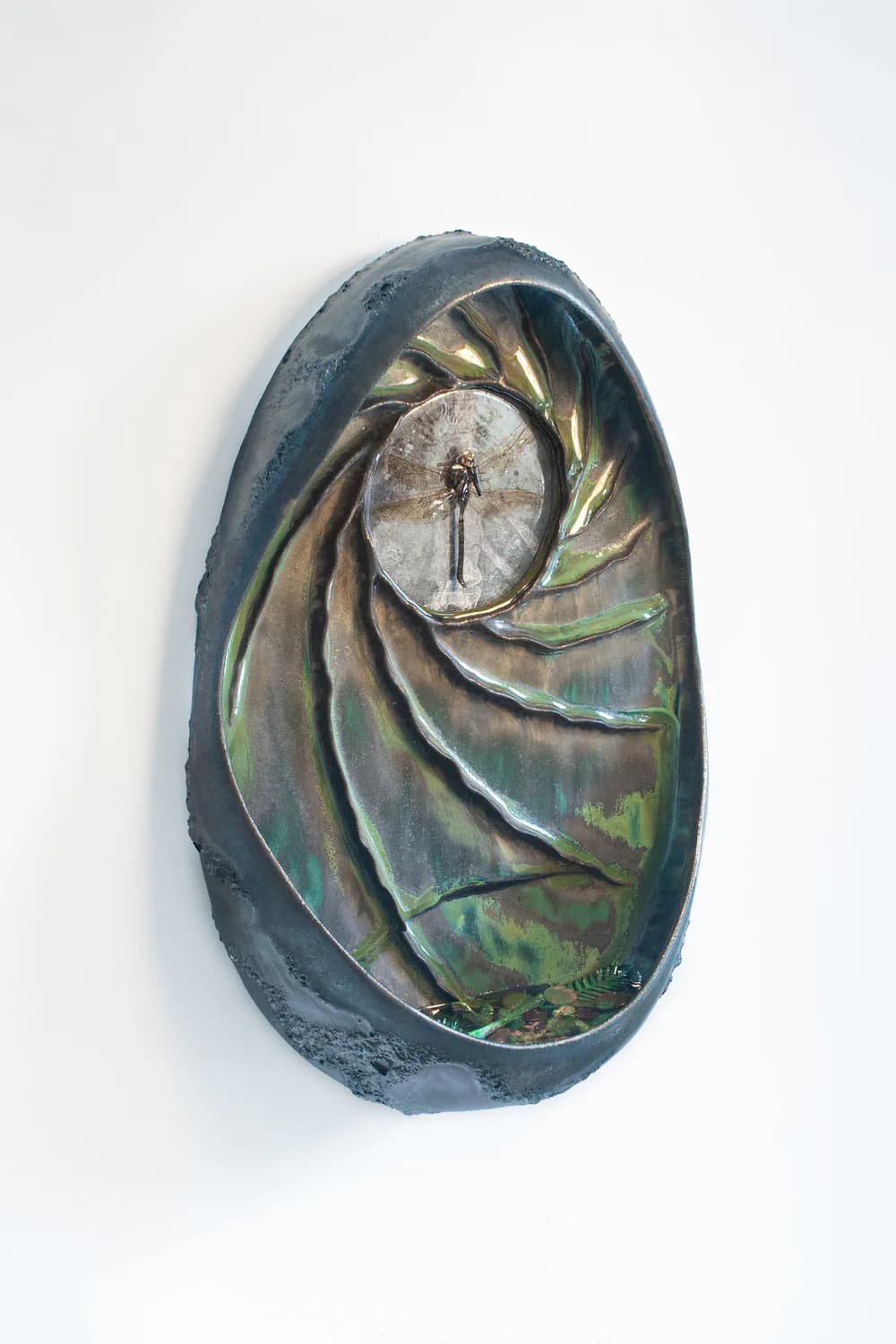 Oval wall sculpture with spiral nautilus form, iridescent green and teal glazes, dragonfly encased in resin at center