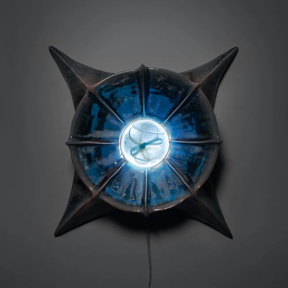 Star-shaped ceramic wall sculpture with glowing blue neon center, illuminated against dark background
