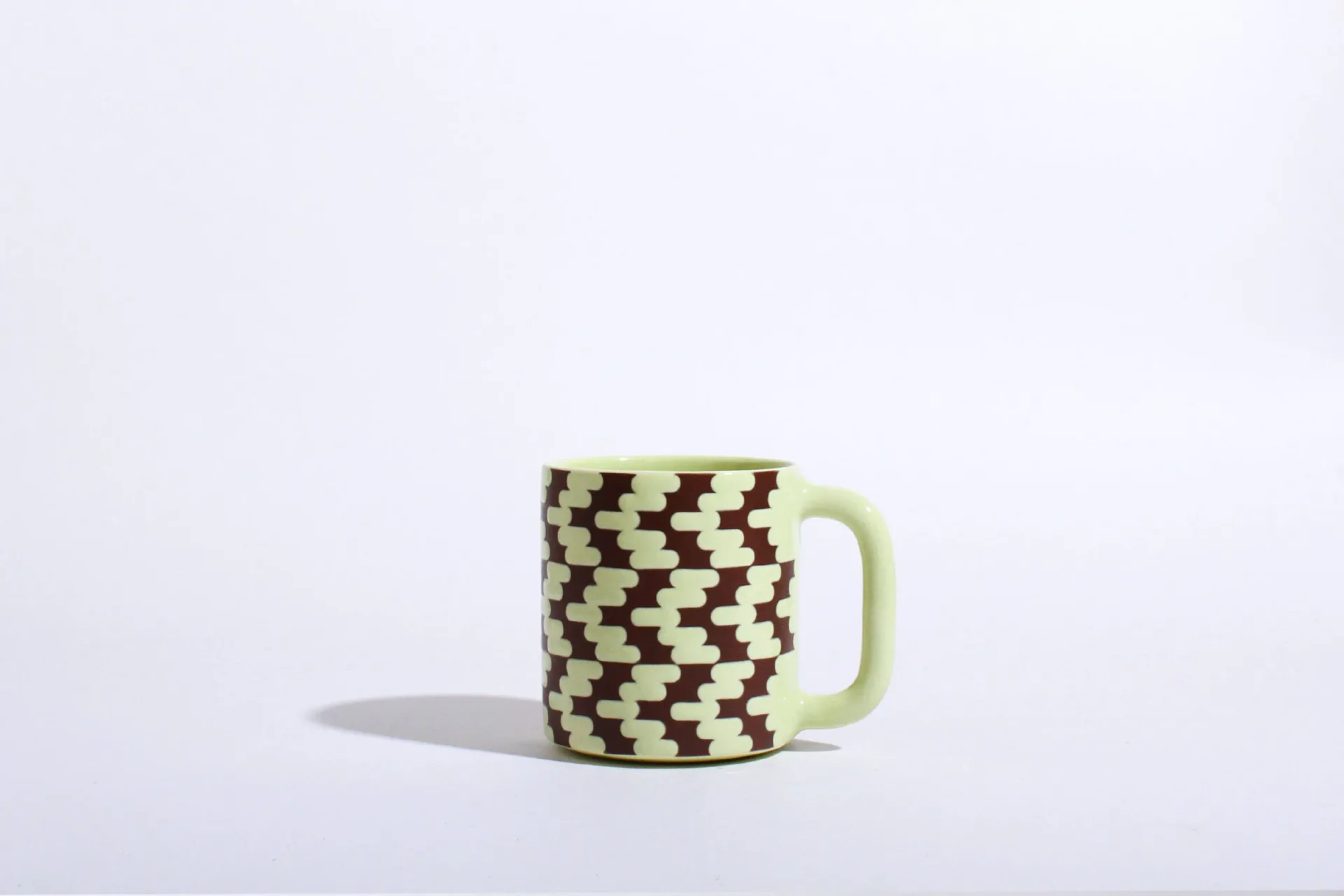 Ceramic mug with brown and chartreuse interlocking capsule/houndstooth geometric pattern
