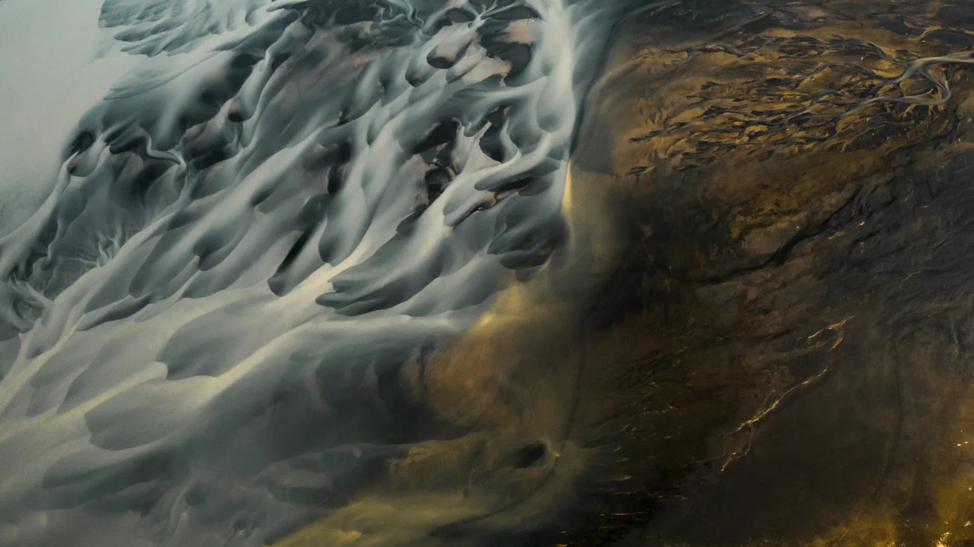 Aerial view of glacial river delta with silver and gold tones