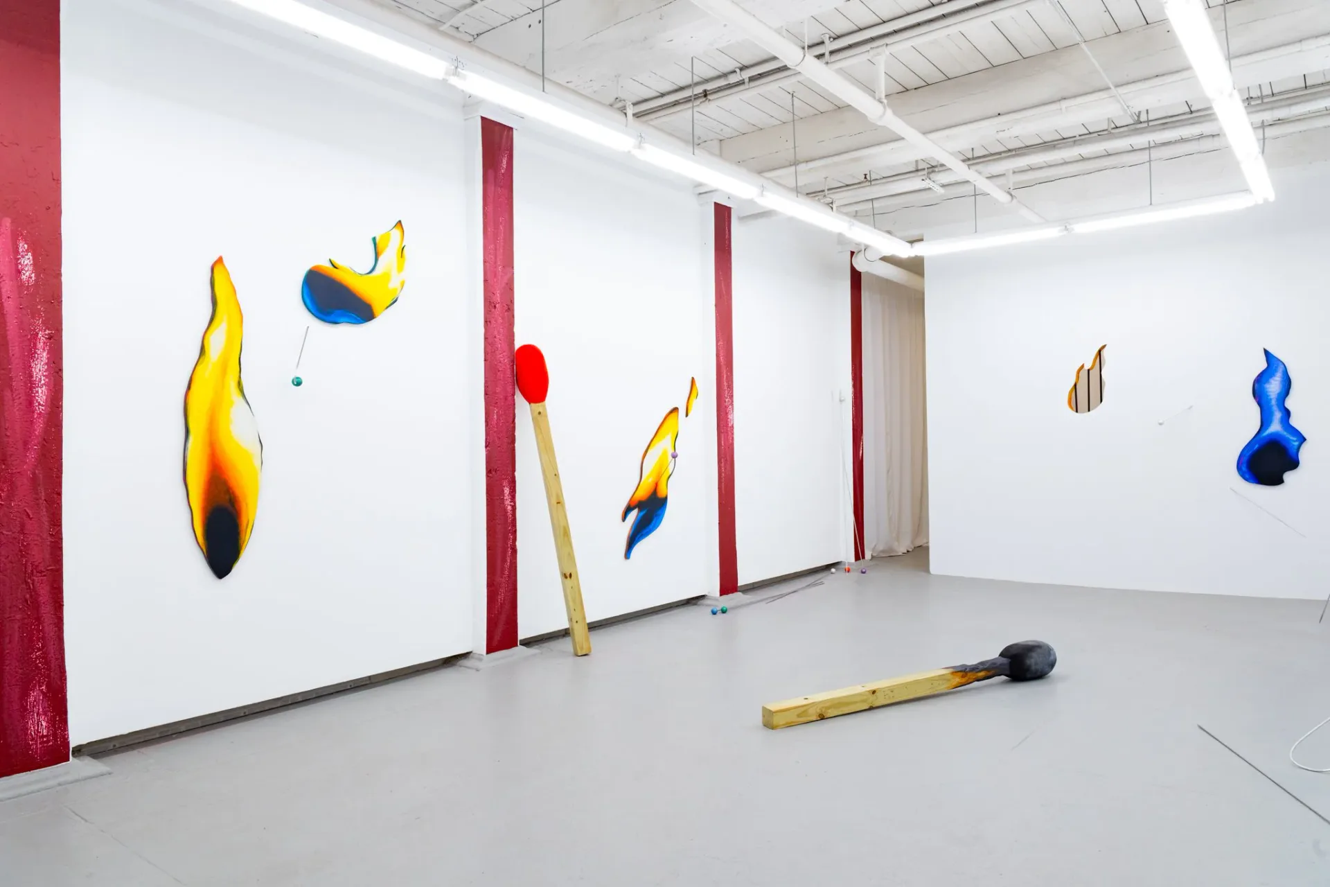 Gallery installation with flame-shaped wall sculptures and match-like floor sculptures with red and dark walls