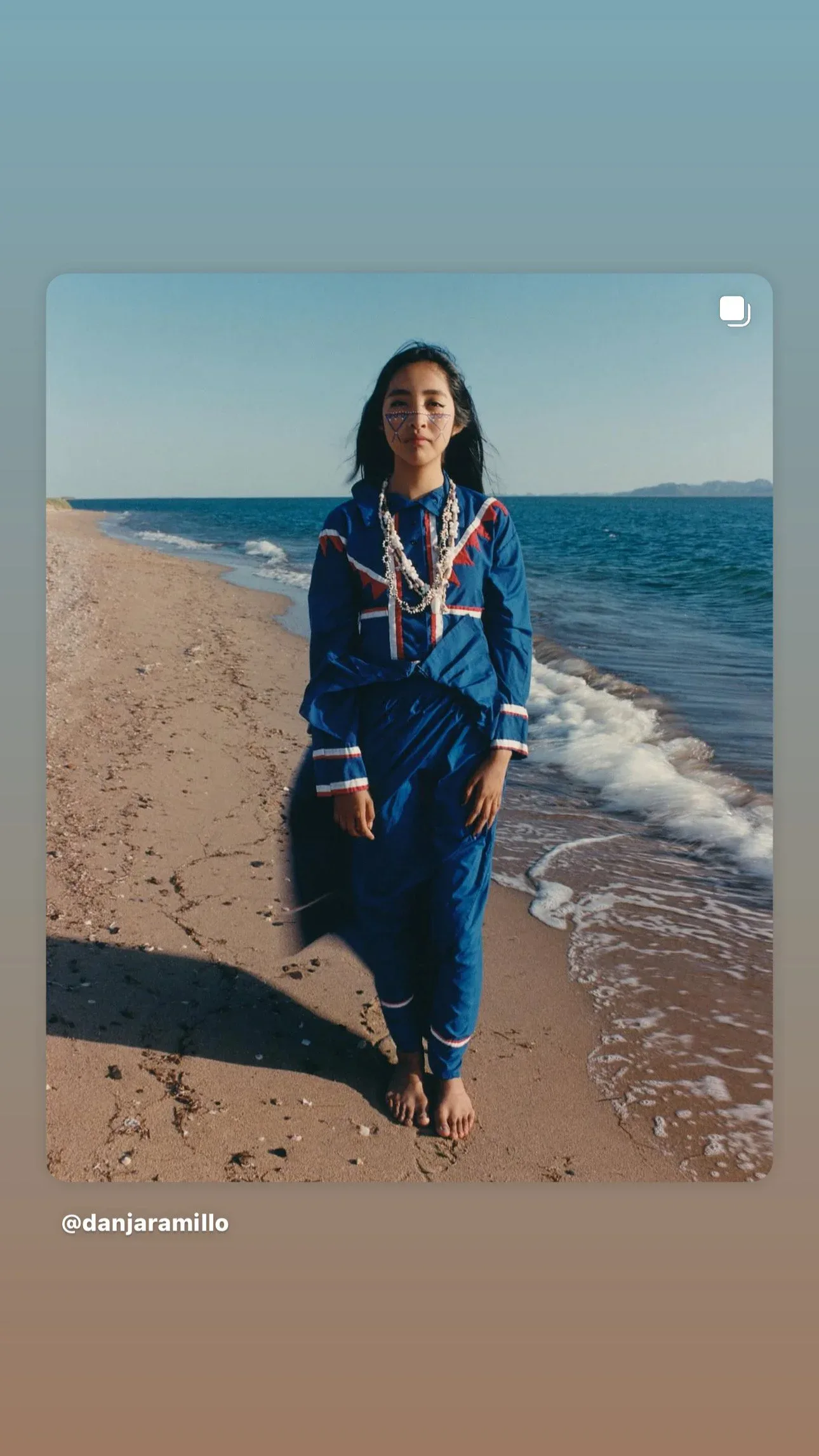 Woman in traditional blue garment with face paint standing on a beach