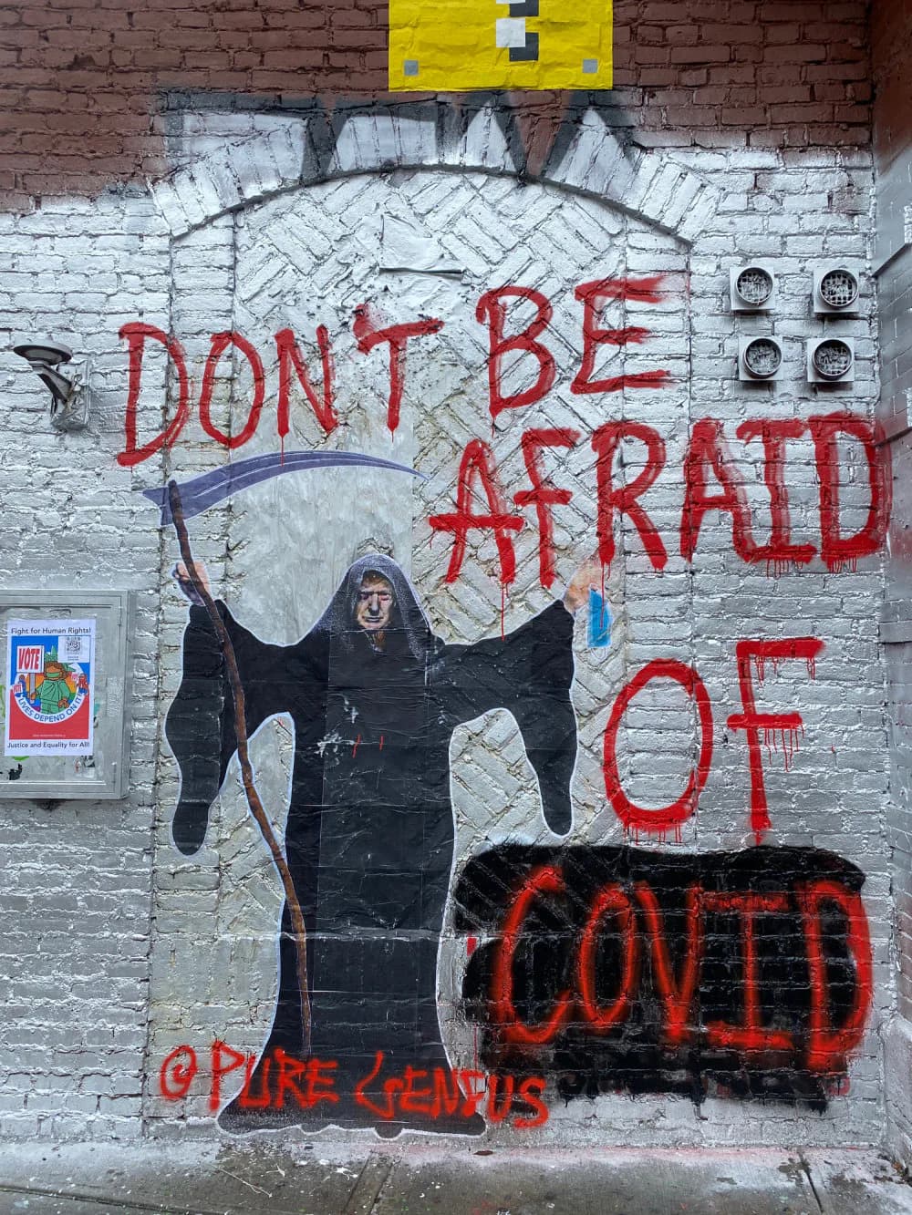 Street mural on white brick featuring dark hooded figure with red text reading 'DON'T BE AFRAID OF' with 'COVID' crossed out, signed Pure Genius.