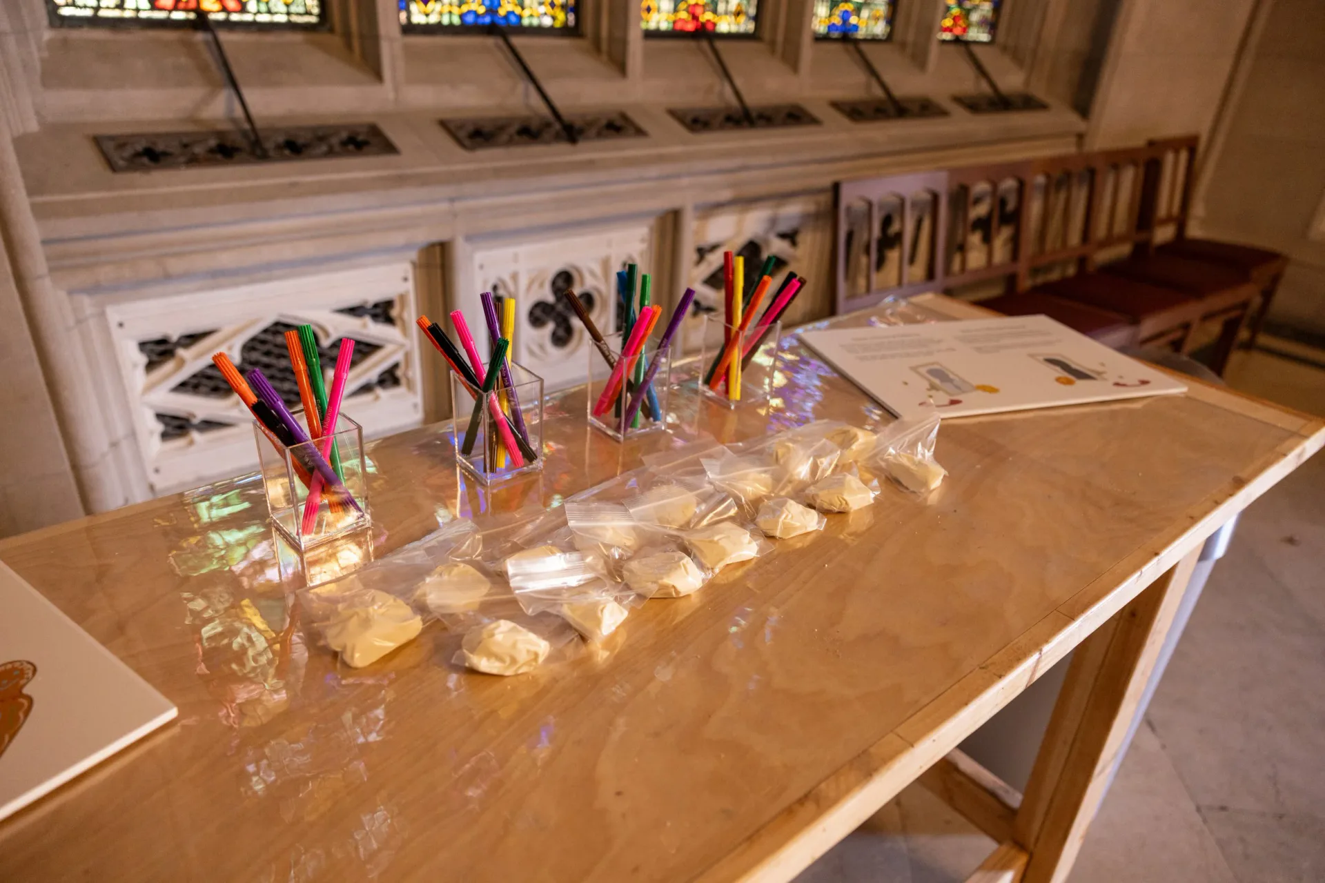 Large panel of cathedral installation showing a figurative painting of a person holding a ceramic vessel surrounded by plant forms, with stained glass and chandelier visible