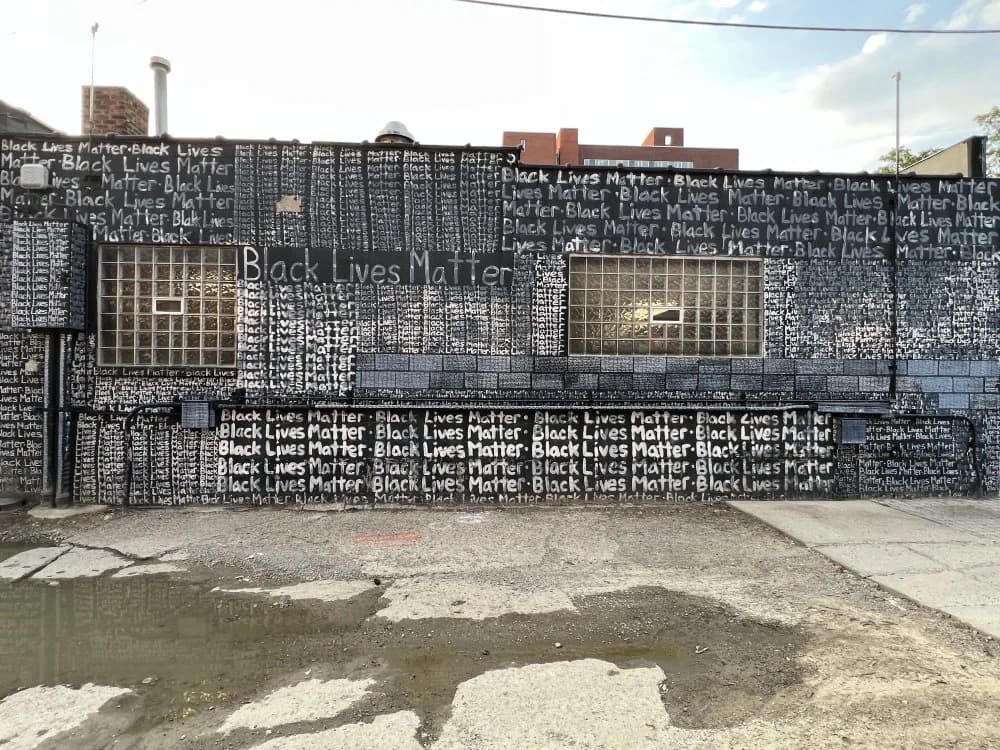 Large-scale metal wall installation with geometric grid pattern and repeated text including "Black Lives Matter," rendered in white and dark tones.