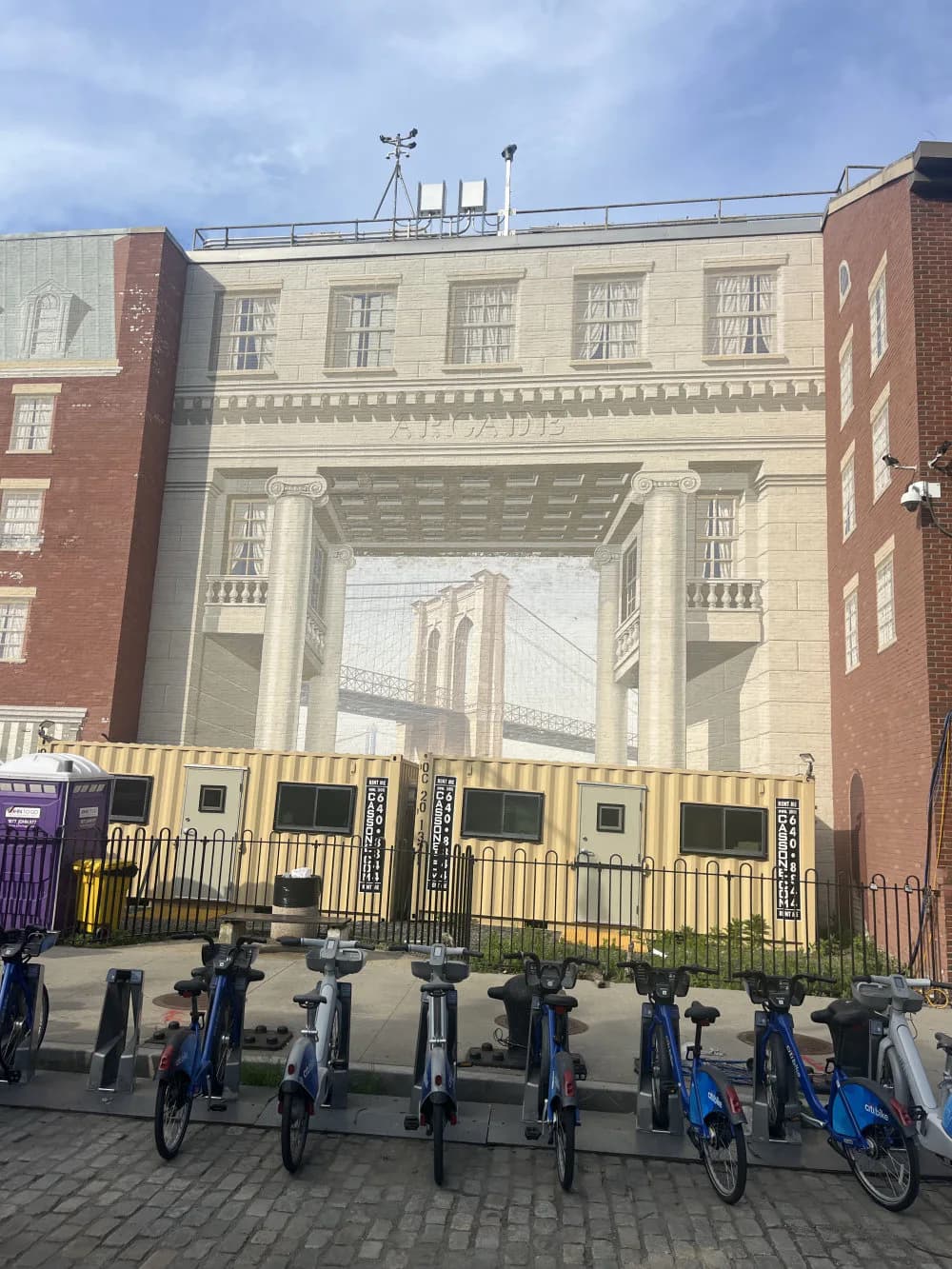 Trompe-l'oeil mural by Richard Haas depicting the Brooklyn Bridge framed within architectural columns, rendered in cream and gray tones on a building facade.
