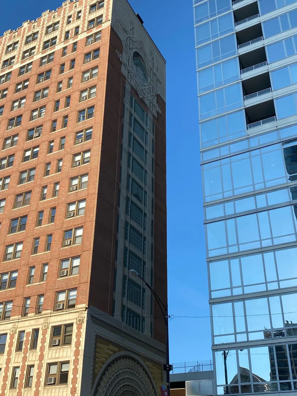 Exterior photograph of two adjacent New York buildings: a terra-cotta brick structure with regular window grid and a modern glass-facade high-rise against blue sky.