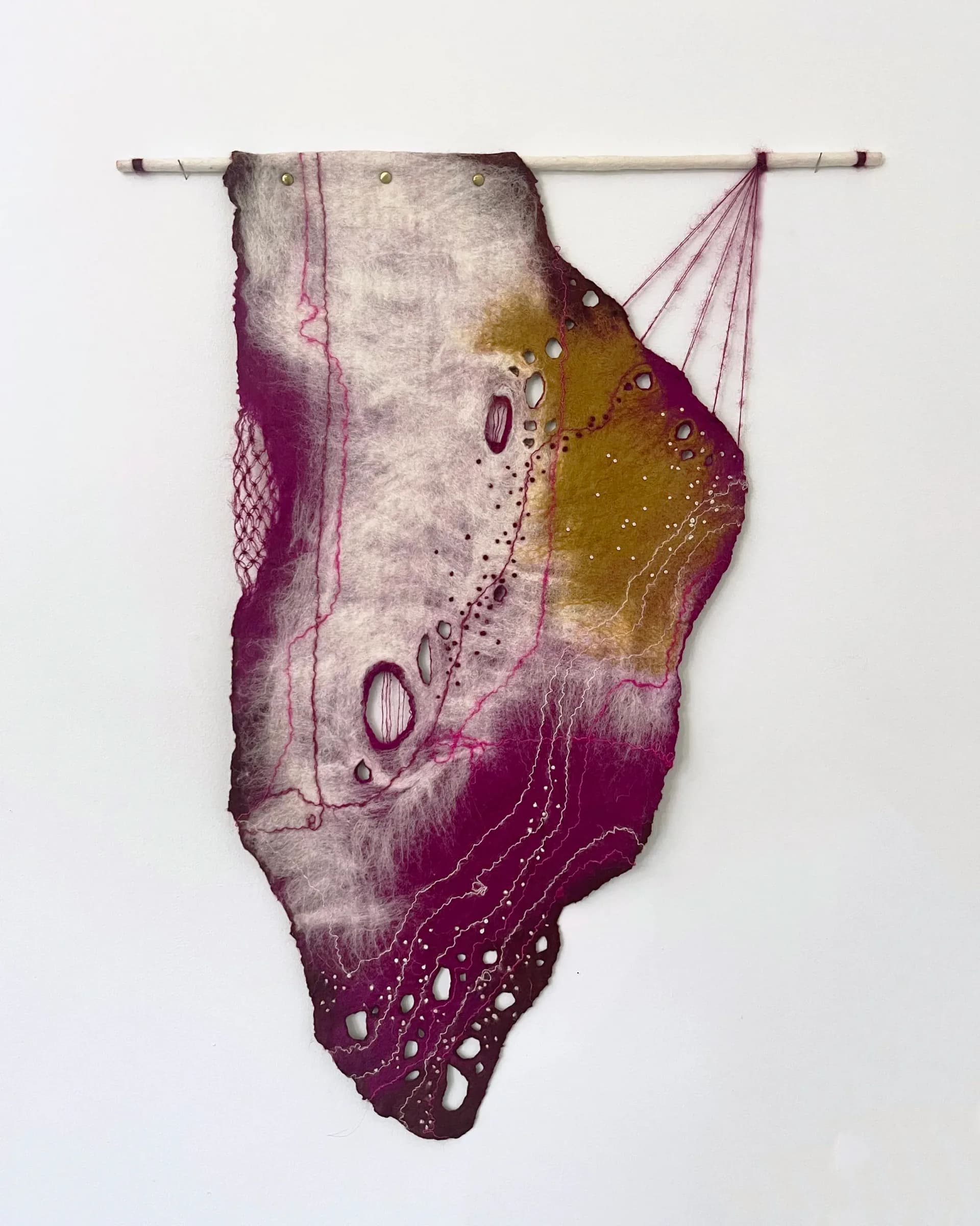 Framed felted textile artwork with magenta, gold, and white tonal gradients and embroidered thread lines, wall-hung on dowel rod