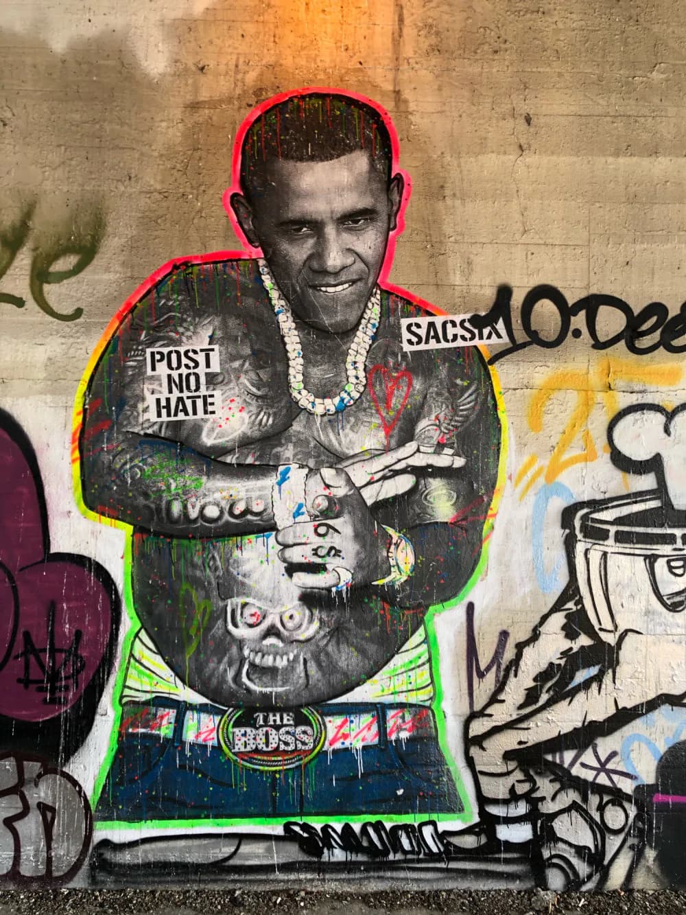 SacSix street art mural showing black-and-white male portrait with red outline, neon-green accents, wearing chain necklace and dark clothing with skull imagery.
