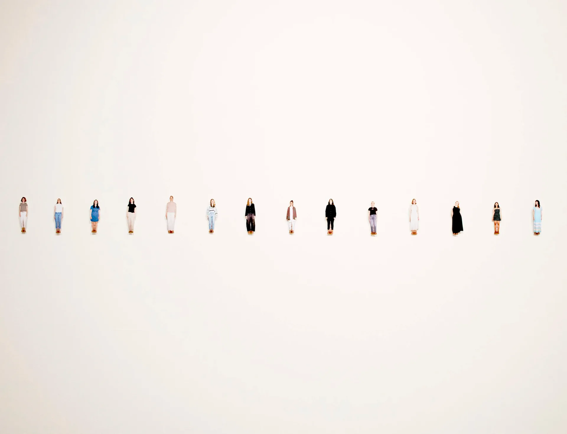 Row of small cut-out figures of women installed on a white gallery wall