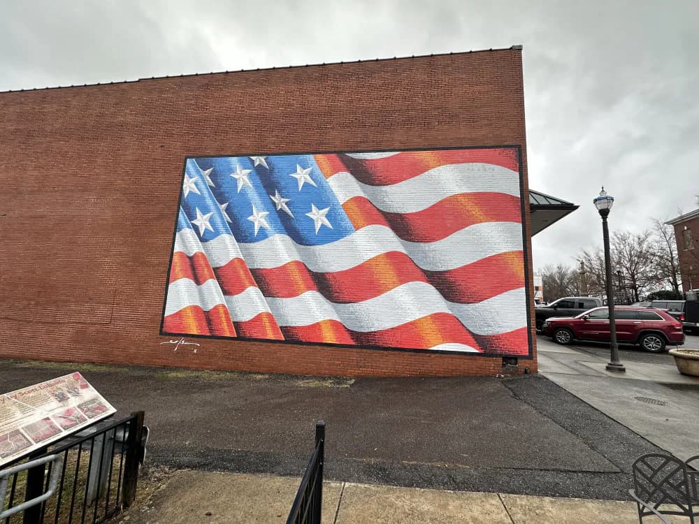 Large-scale mural on brick wall depicting an American flag with flowing, dynamic waves in red, white, and blue.