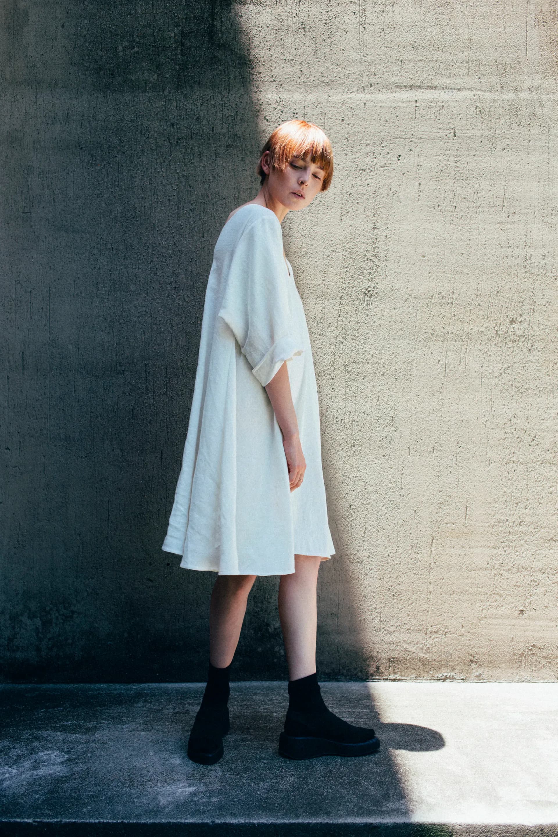 Fashion photography: model in white dress against textured concrete wall with strong directional light