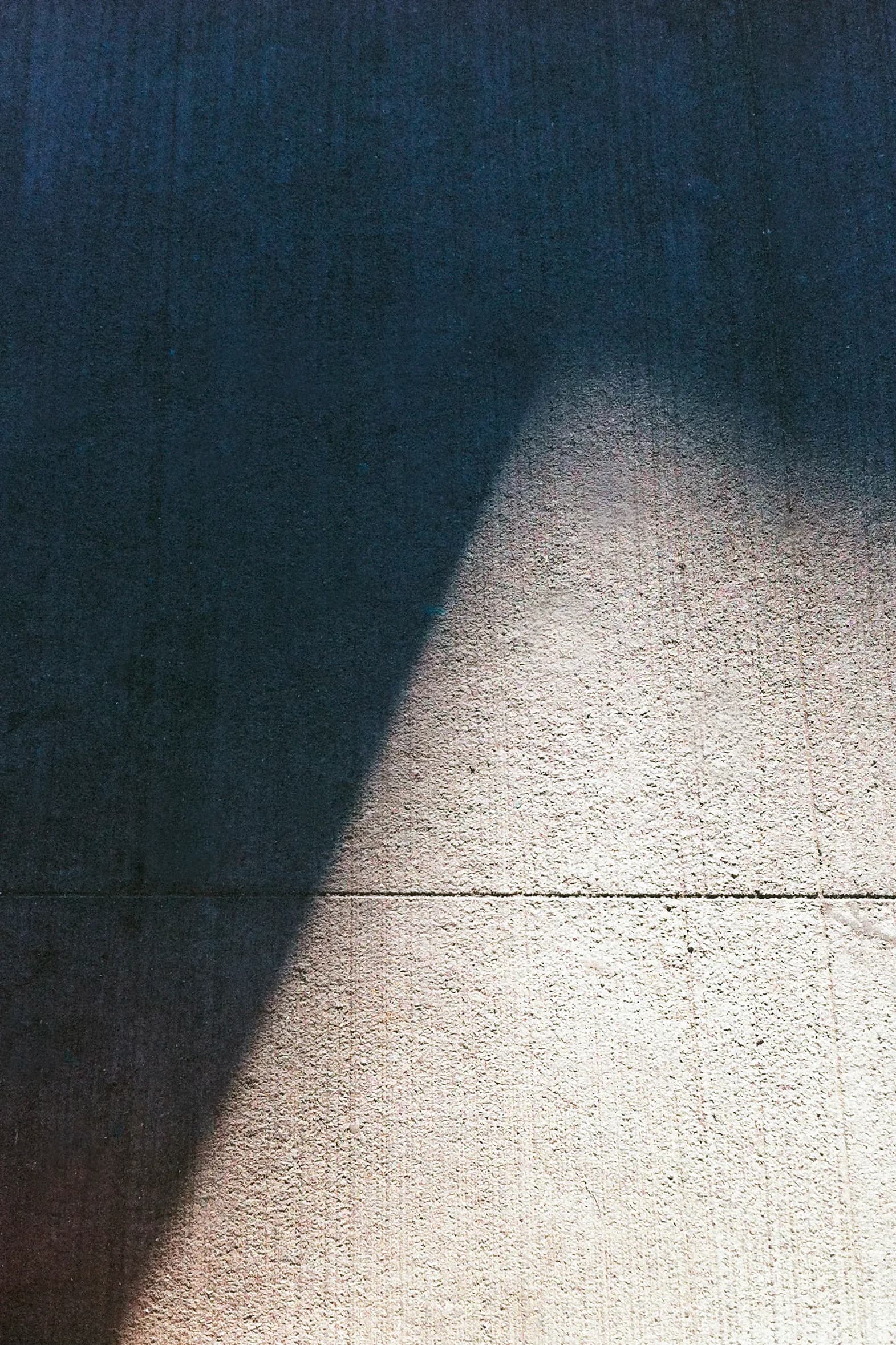 Abstract photography of diagonal shadow cast across concrete wall and floor in deep teal and warm tones