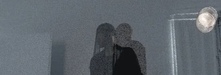 Atmospheric grainy photograph of two figures embracing, rendered in grey tones with a soft overhead light