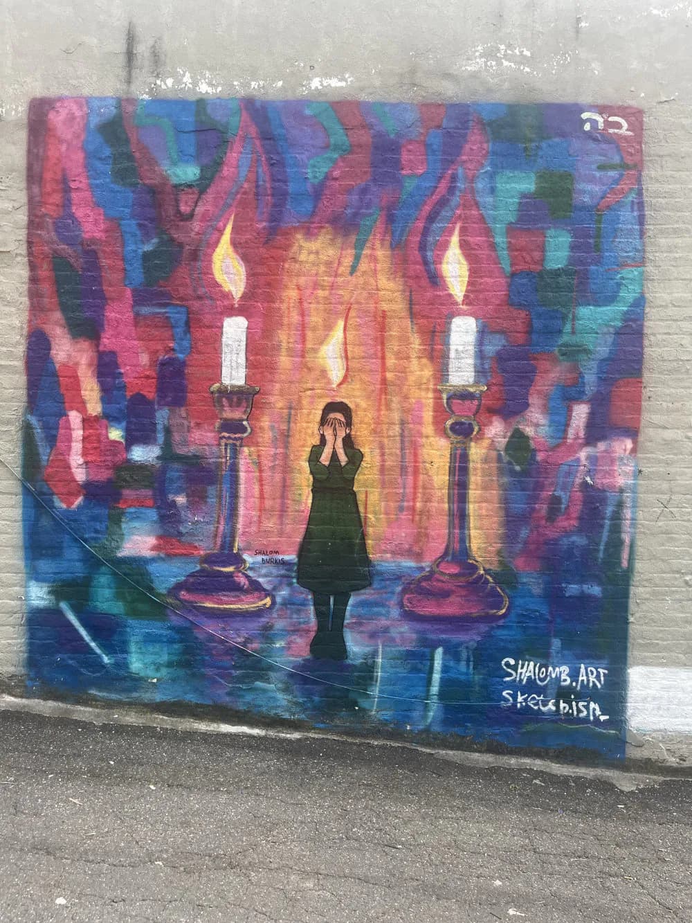 Mixed-media mural by Shalom Burkis featuring a silhouetted figure surrounded by candles and vibrant pink, blue, and red abstract flames on dark background.