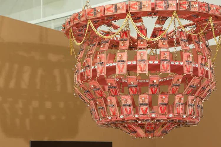 Red and pink tiered chandelier installation with gold beaded swags and hanging elements against a neutral wall.