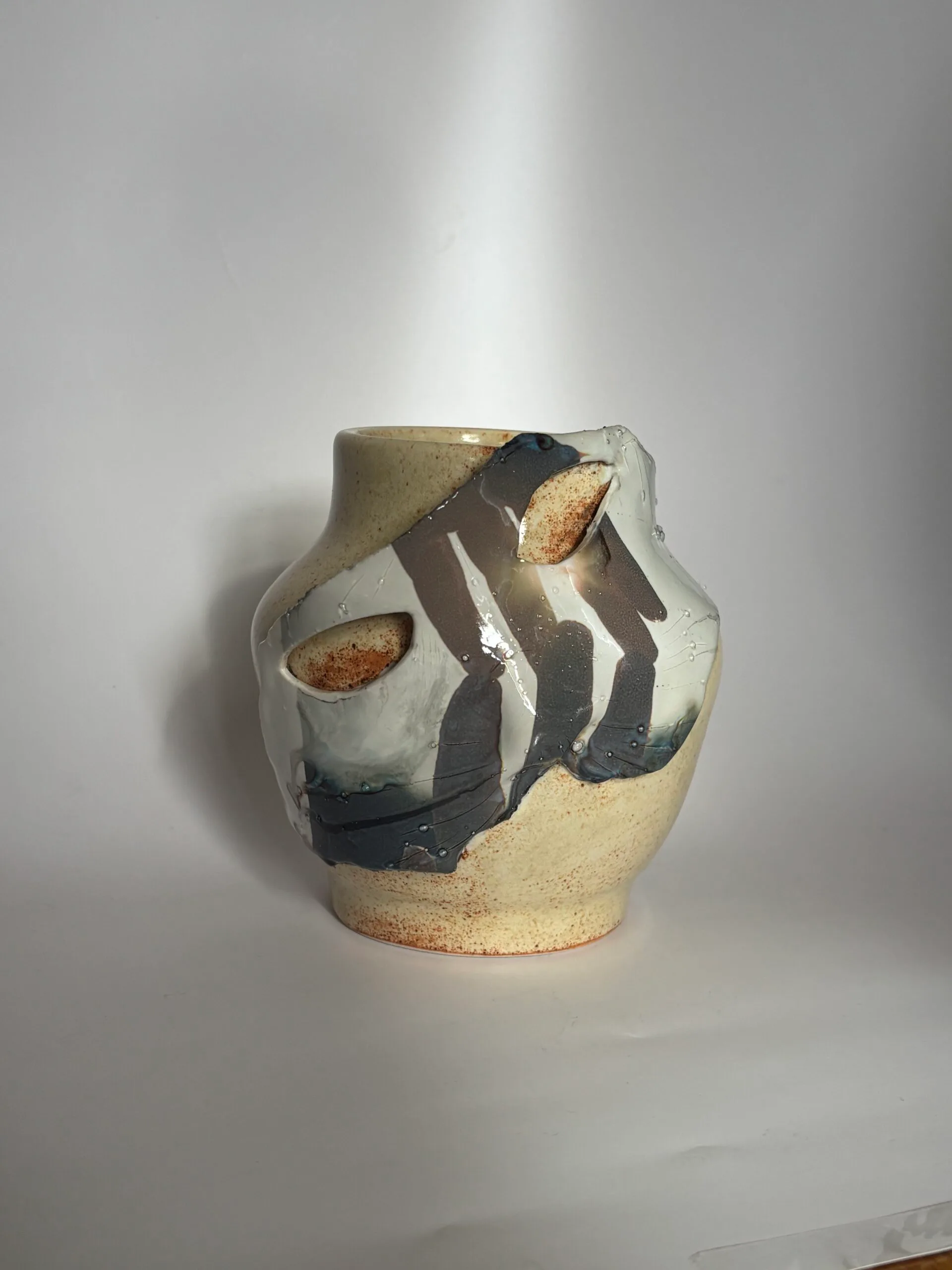 Ceramic pottery vessel with off-white and tan glaze, featuring bold dark brushstrokes and open cutwork sections.