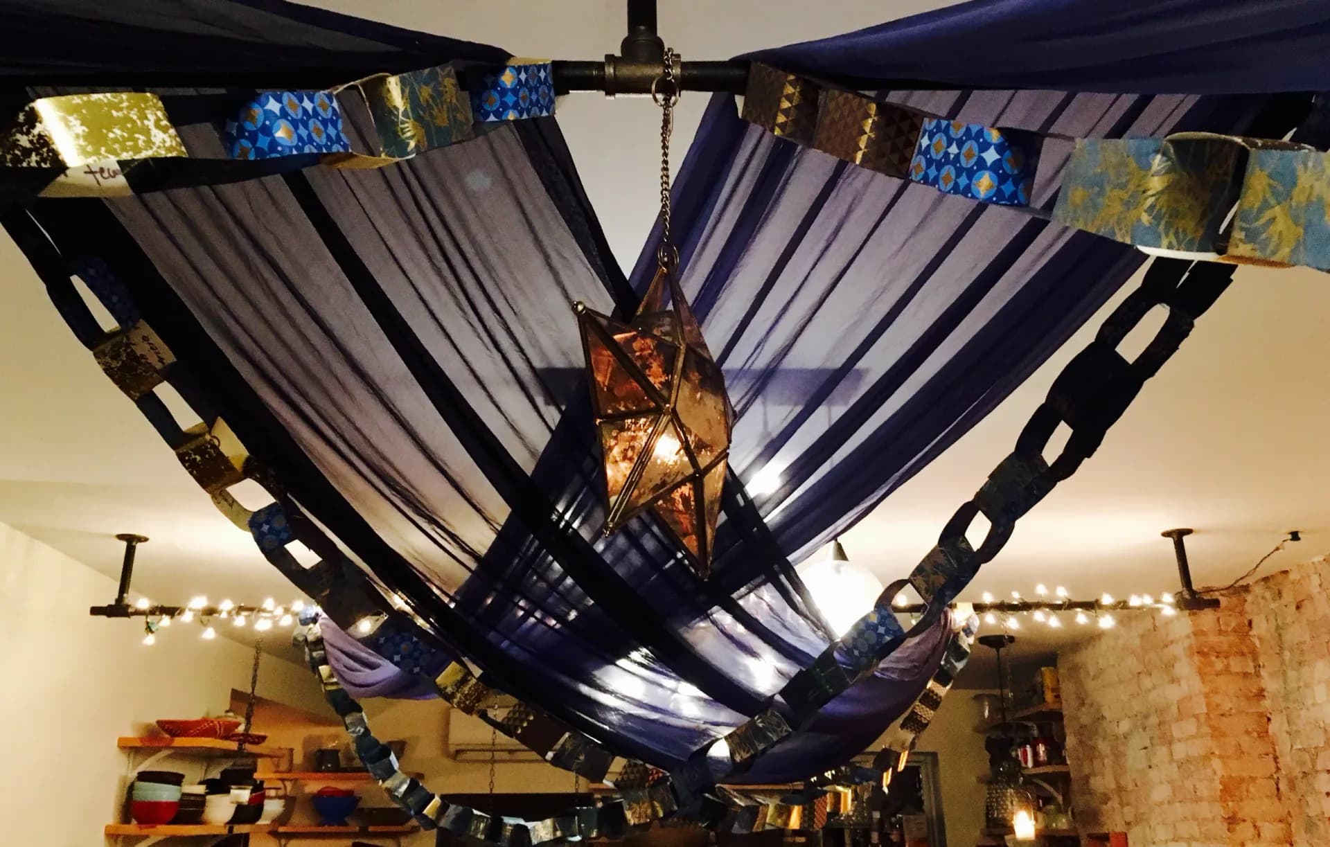 Blue draped fabric canopy with star lantern and patterned garlands hanging from ceiling