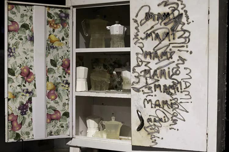 White cabinet with floral-patterned doors and shelves displaying ceramic vessels and kitchenware; right door features black graffiti-style text overlay.