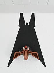 Bat-form relief sculpture with geometric patterning in black, orange, and grey mounted on wall