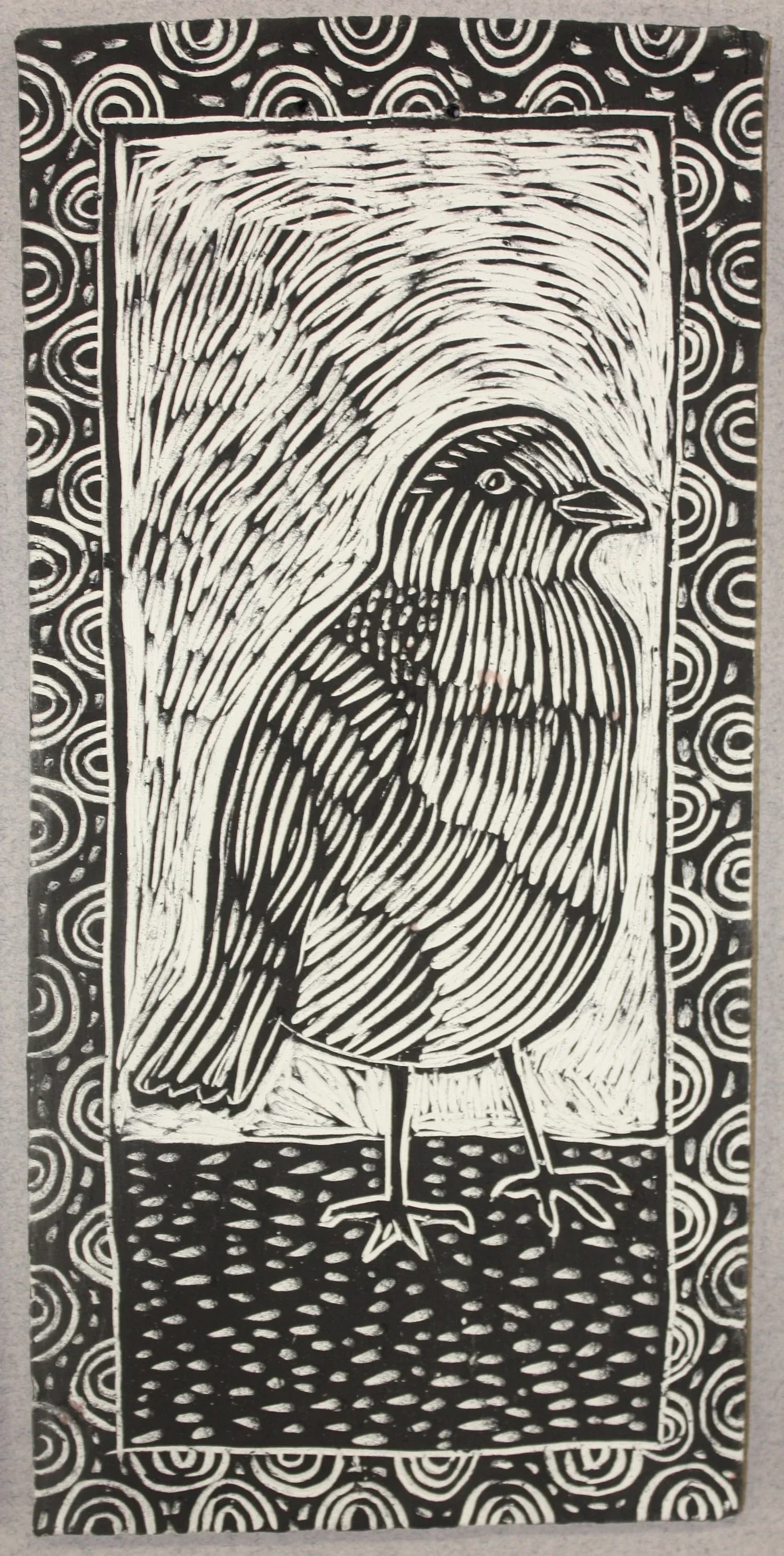 Black and white linocut or sgraffito ceramic tile of a bird with spiral border pattern