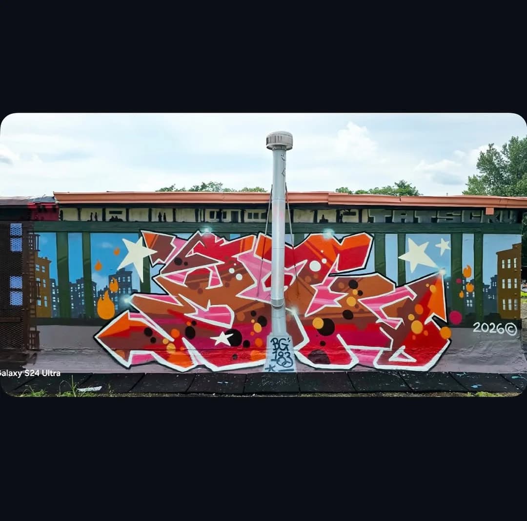 Large-scale graffiti mural on building wall with abstract red, orange, and yellow wildstyle lettering and skyline silhouettes, dated 2026.