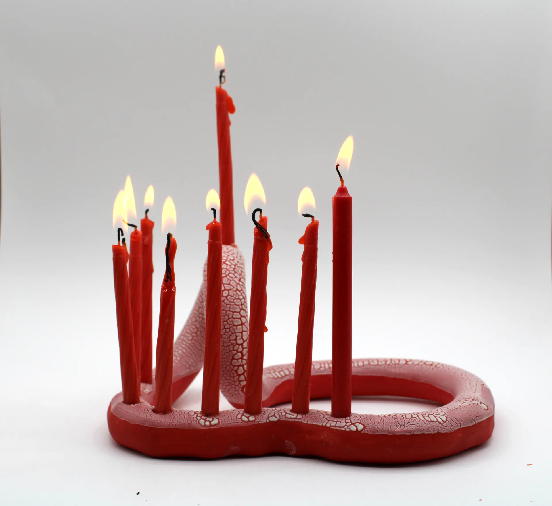 Red snake-form candelabra with lit red candles and crackle glaze texture