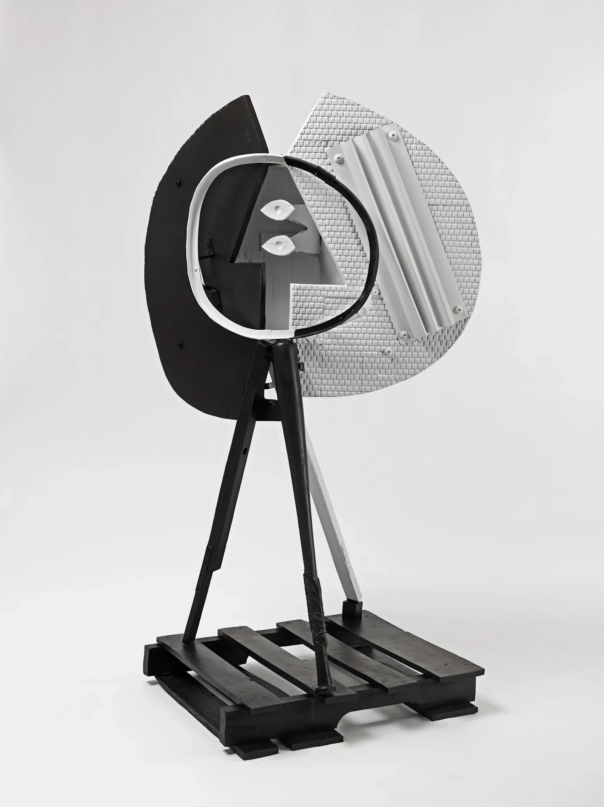 Black and white sculptural fan installation with curved panels, tripod legs, and metal framework on rectangular base.