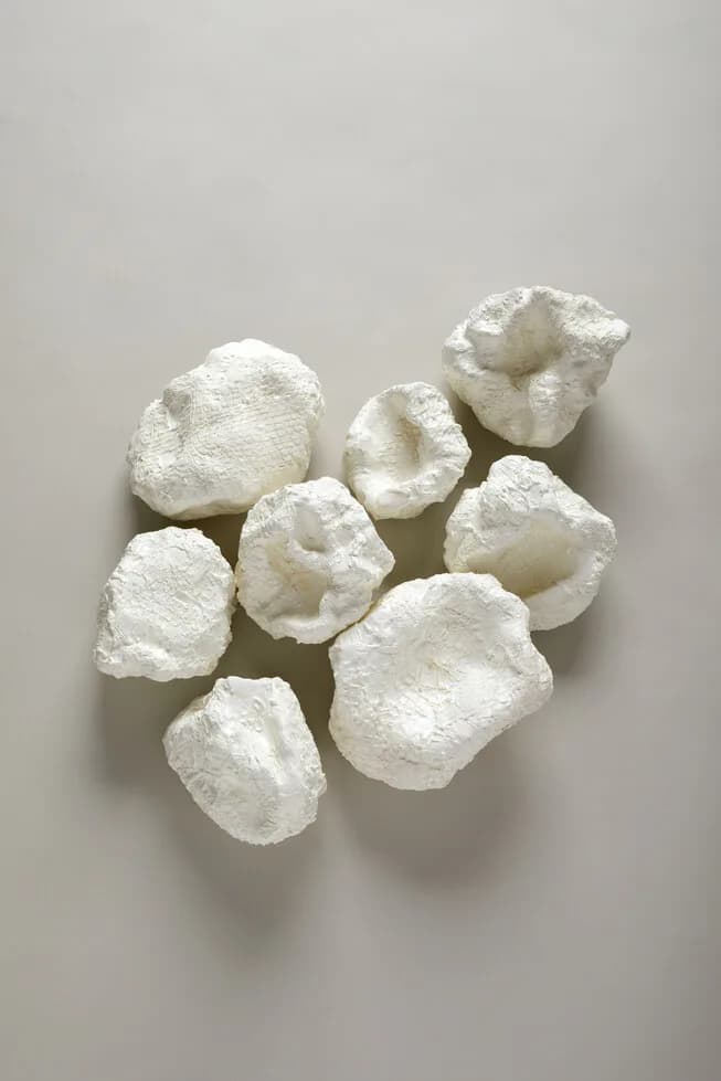 Four white sculptural forms suspended in mid-air against a neutral grey background