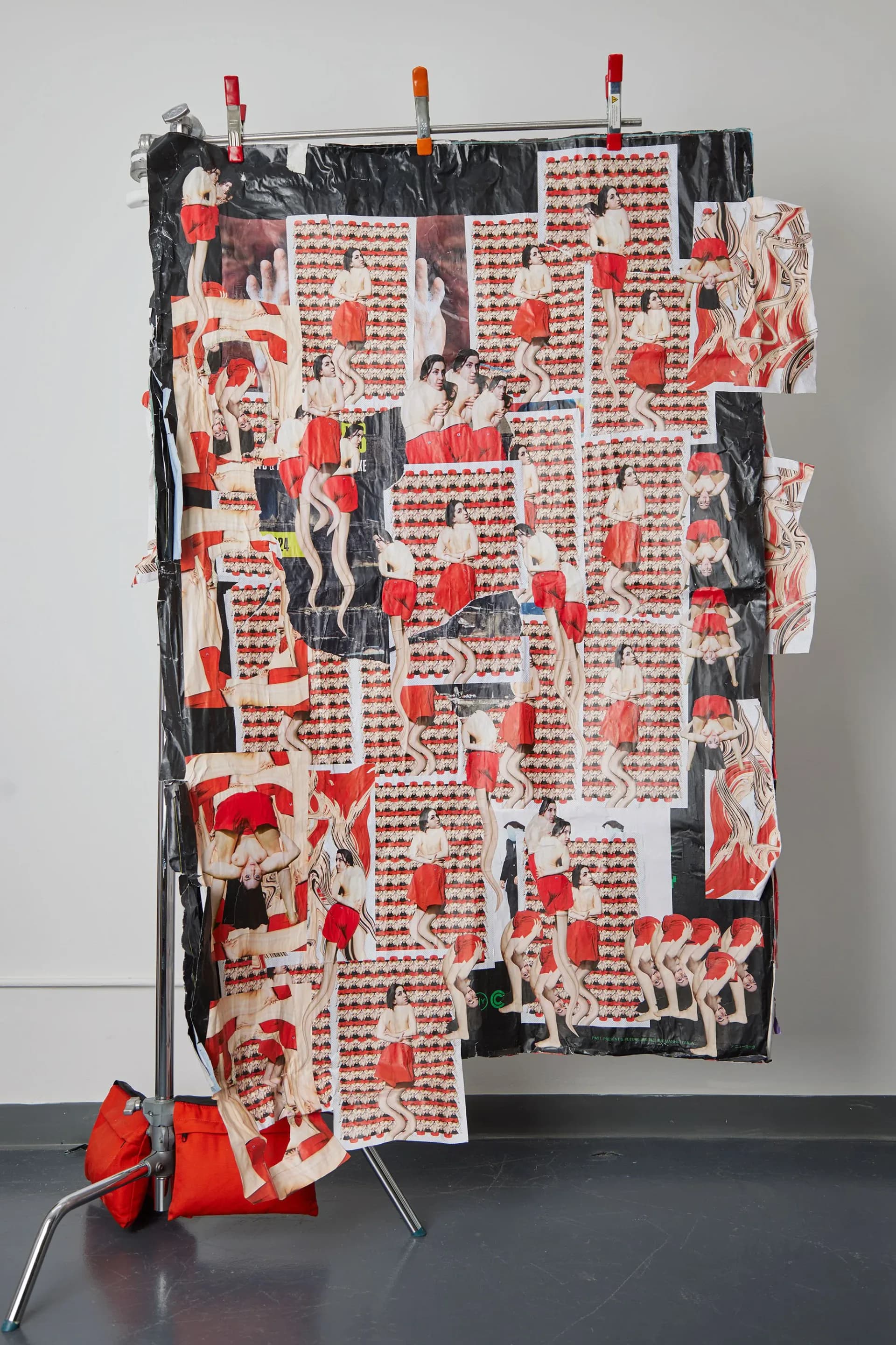 Large-scale collage work with repeated green alien-masked figures and colorful imagery hung on a stand